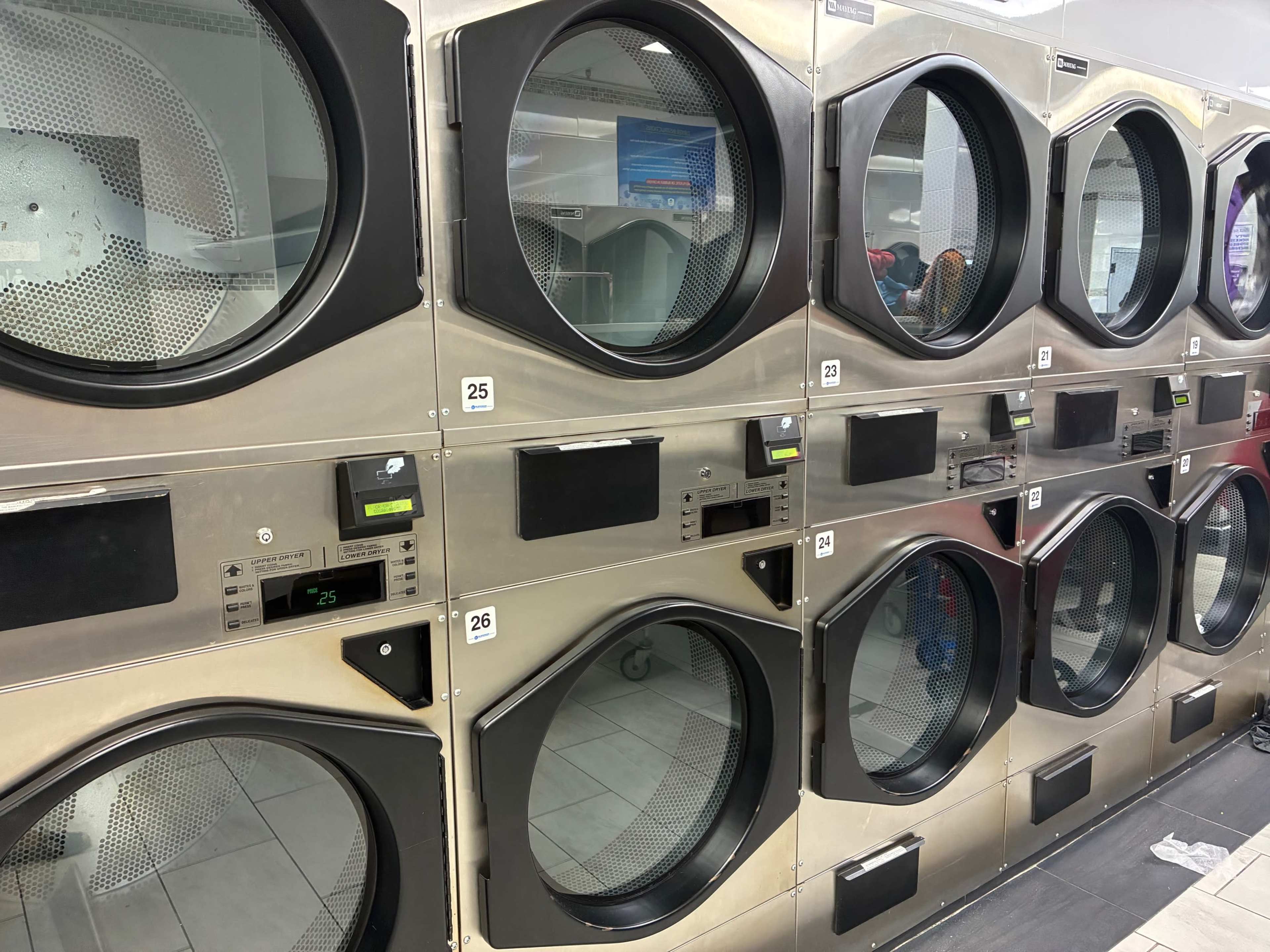 The image shows a row of industrial dryers in a laundromat, with several units displaying digital control panels.