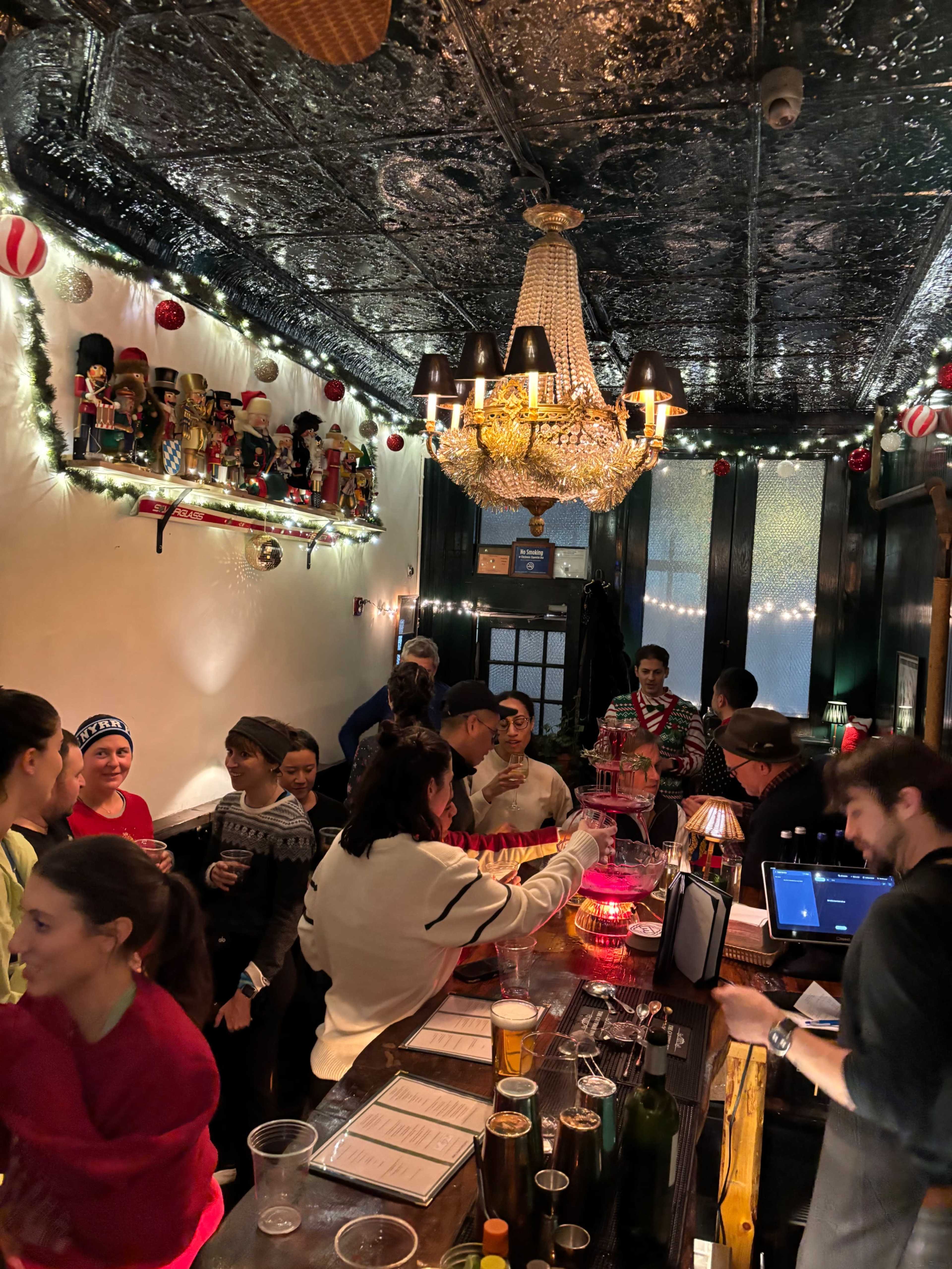 A crowded bar with festive decorations, including nutcracker figures and string lights, with patrons engaged in conversation and bartenders preparing drinks.