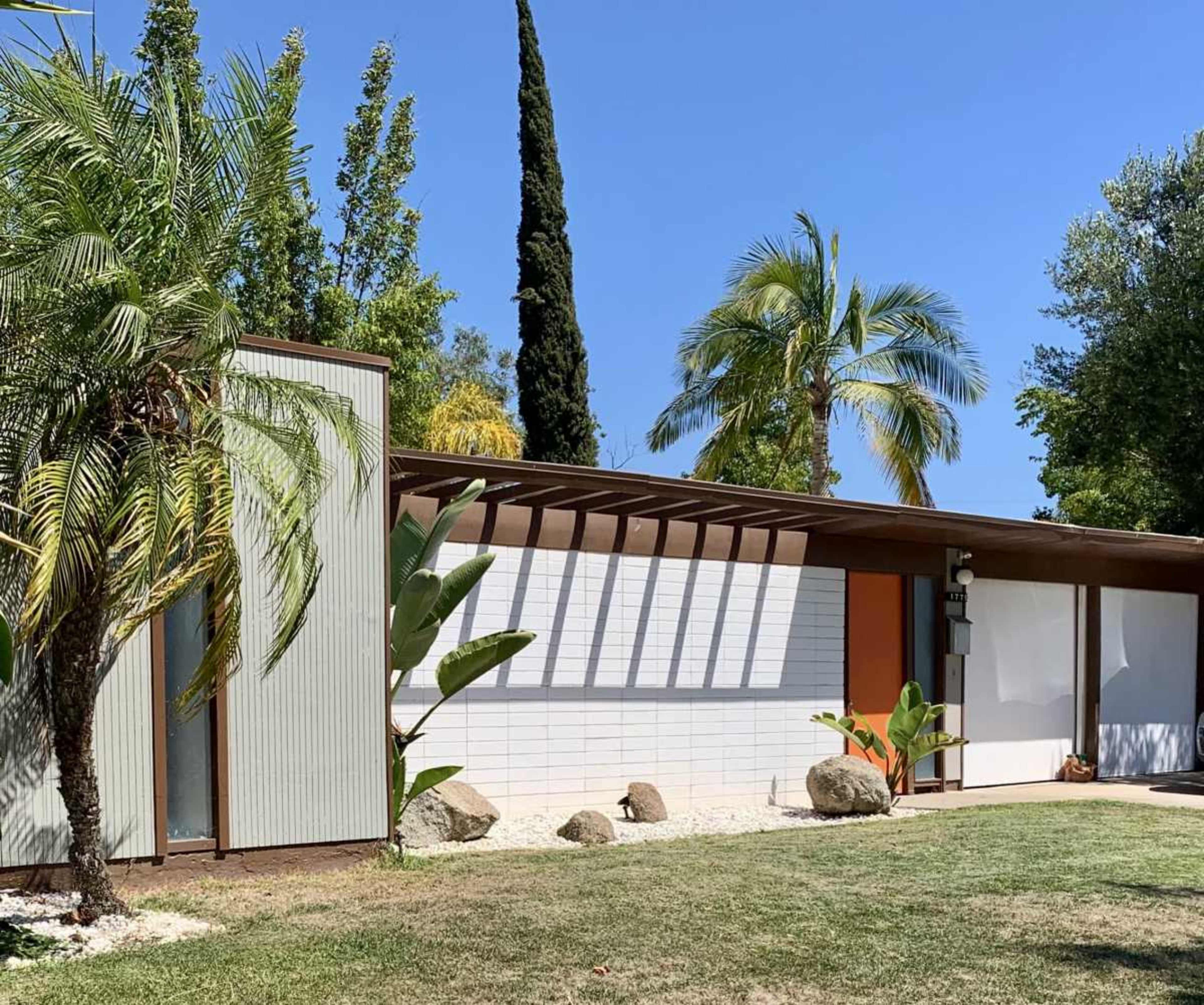 A mid-century modern house featuring a combination of textured walls, a flat roof, and tropical landscaping.