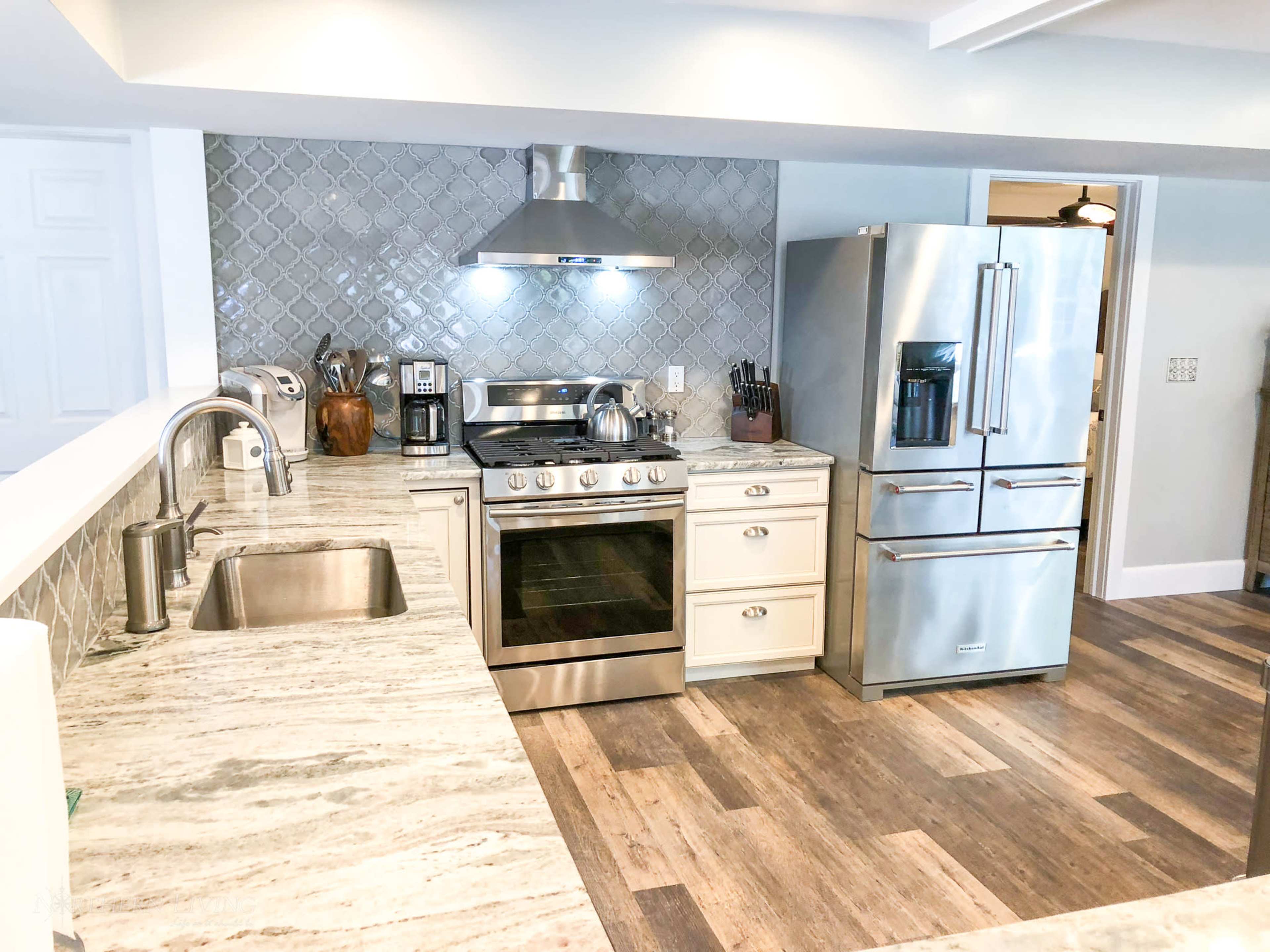 A modern kitchen featuring stainless steel appliances, including a stove and refrigerator, with a light-colored countertop and a backsplash of patterned tiles.