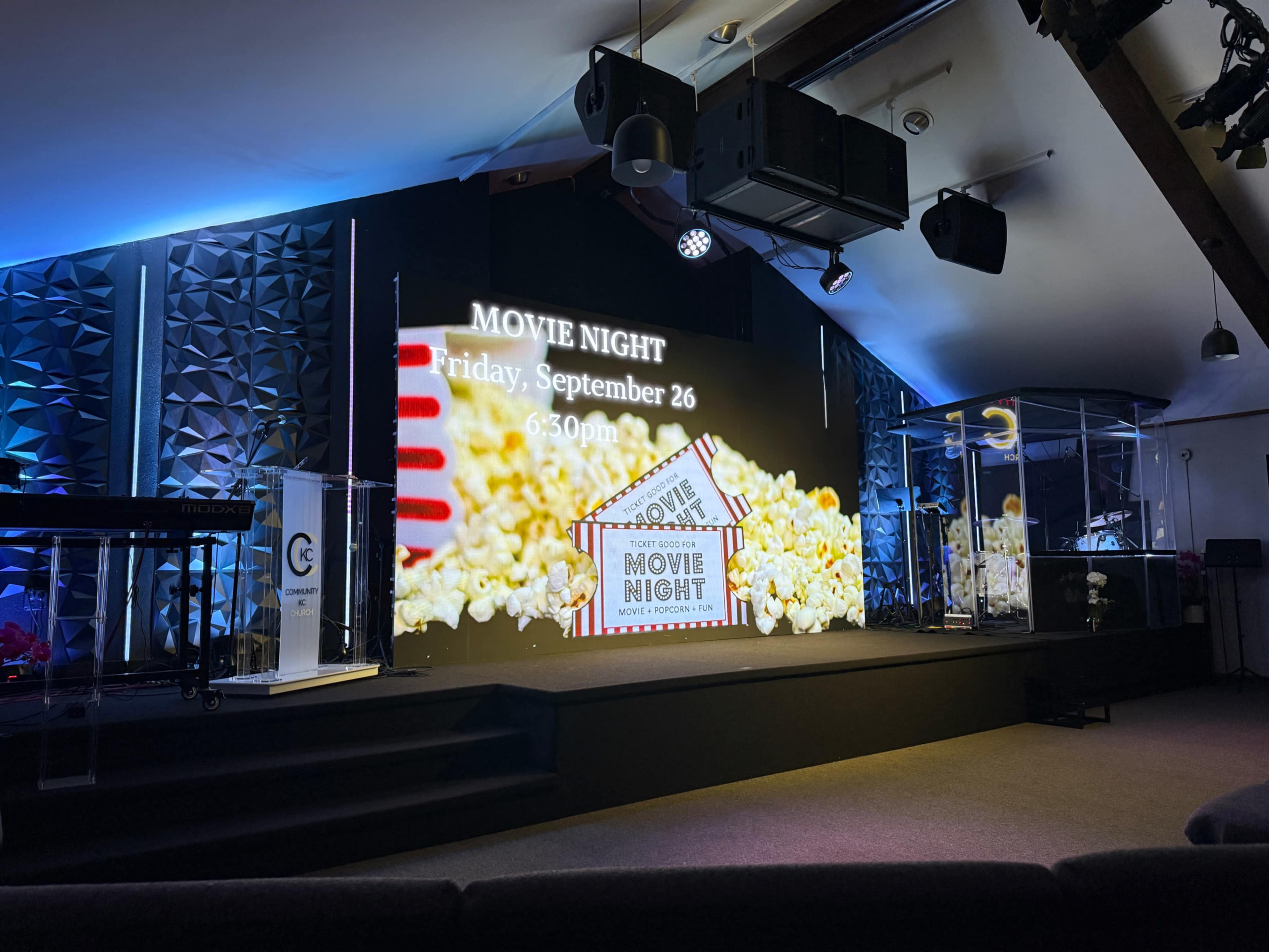 A stage is set for a movie night event, featuring a large screen displaying the event details with popcorn images in the background.