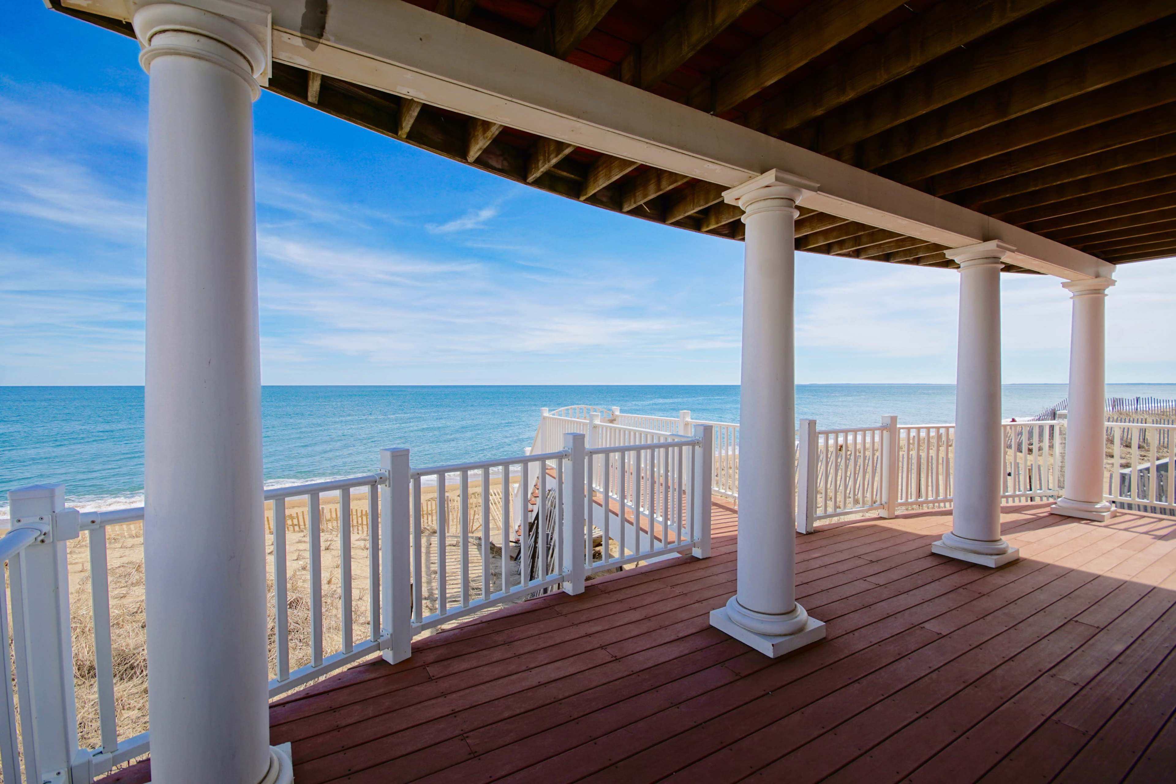 A covered porch with white columns overlooking a sandy beach and the ocean.