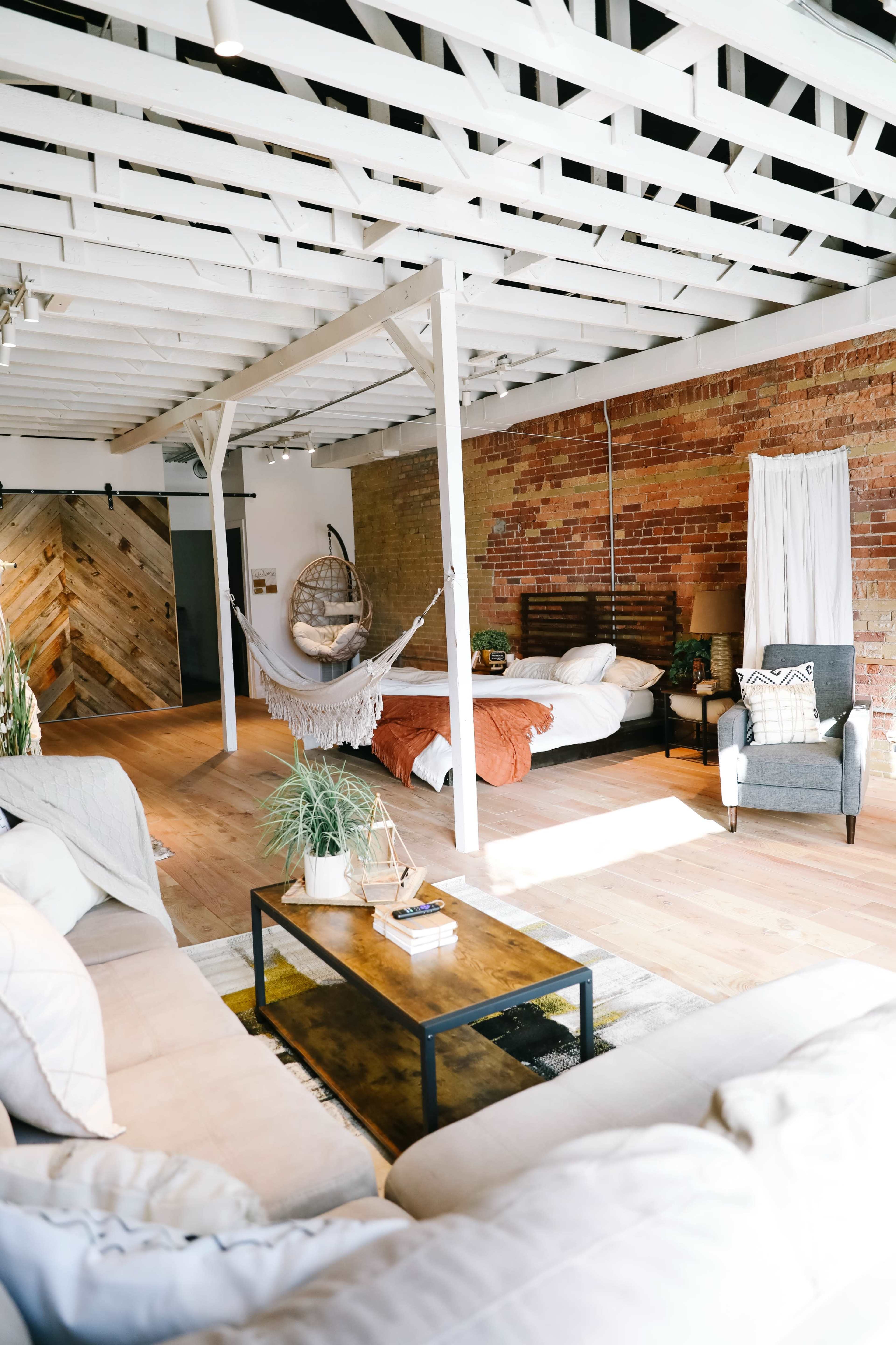 A spacious, open-layout living area with a seating area, a hammock, and a bed, all featuring wooden elements and a mix of brick and wood decor.