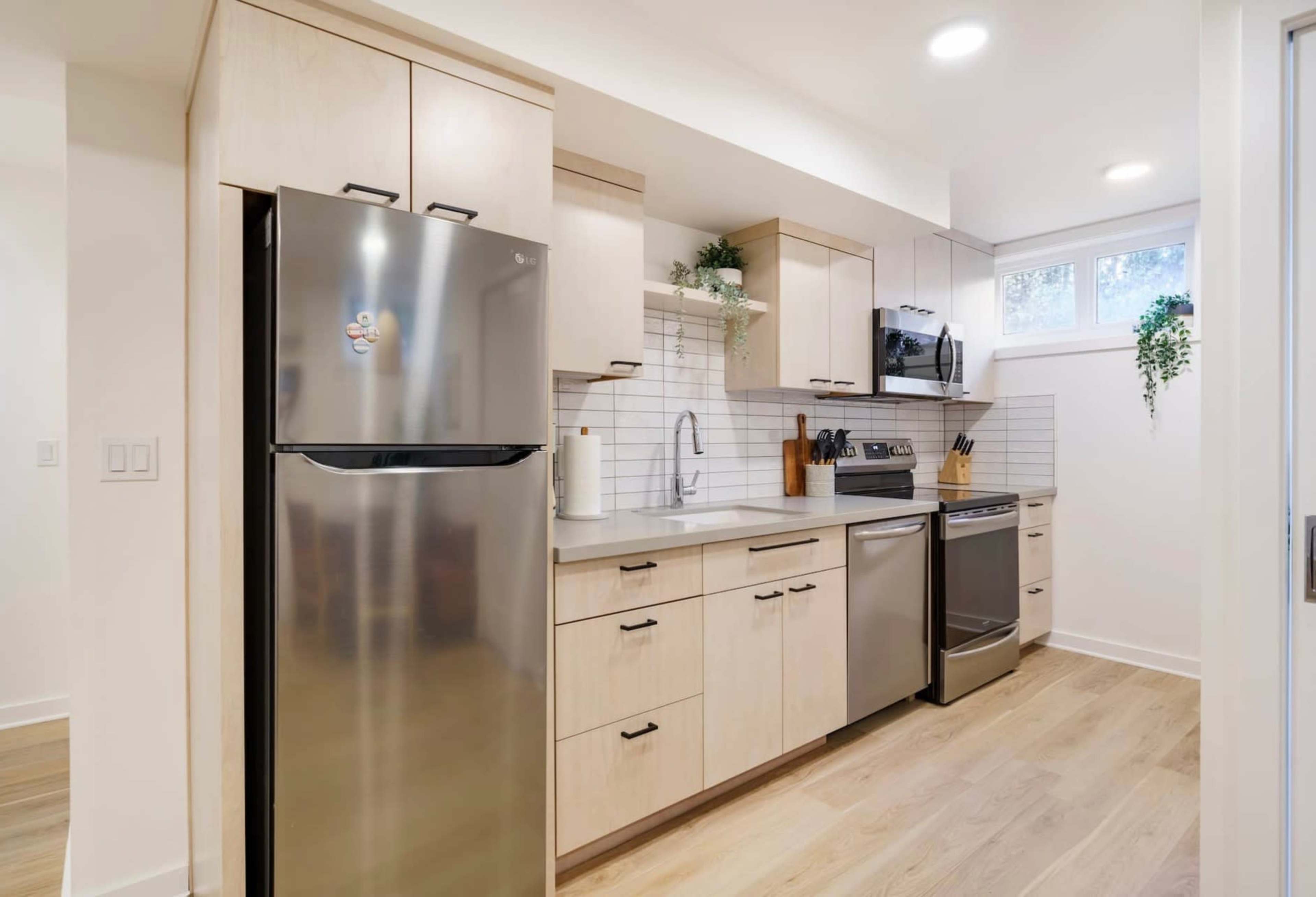A modern kitchen with stainless steel appliances, light wood cabinetry, and white tiled backsplash.