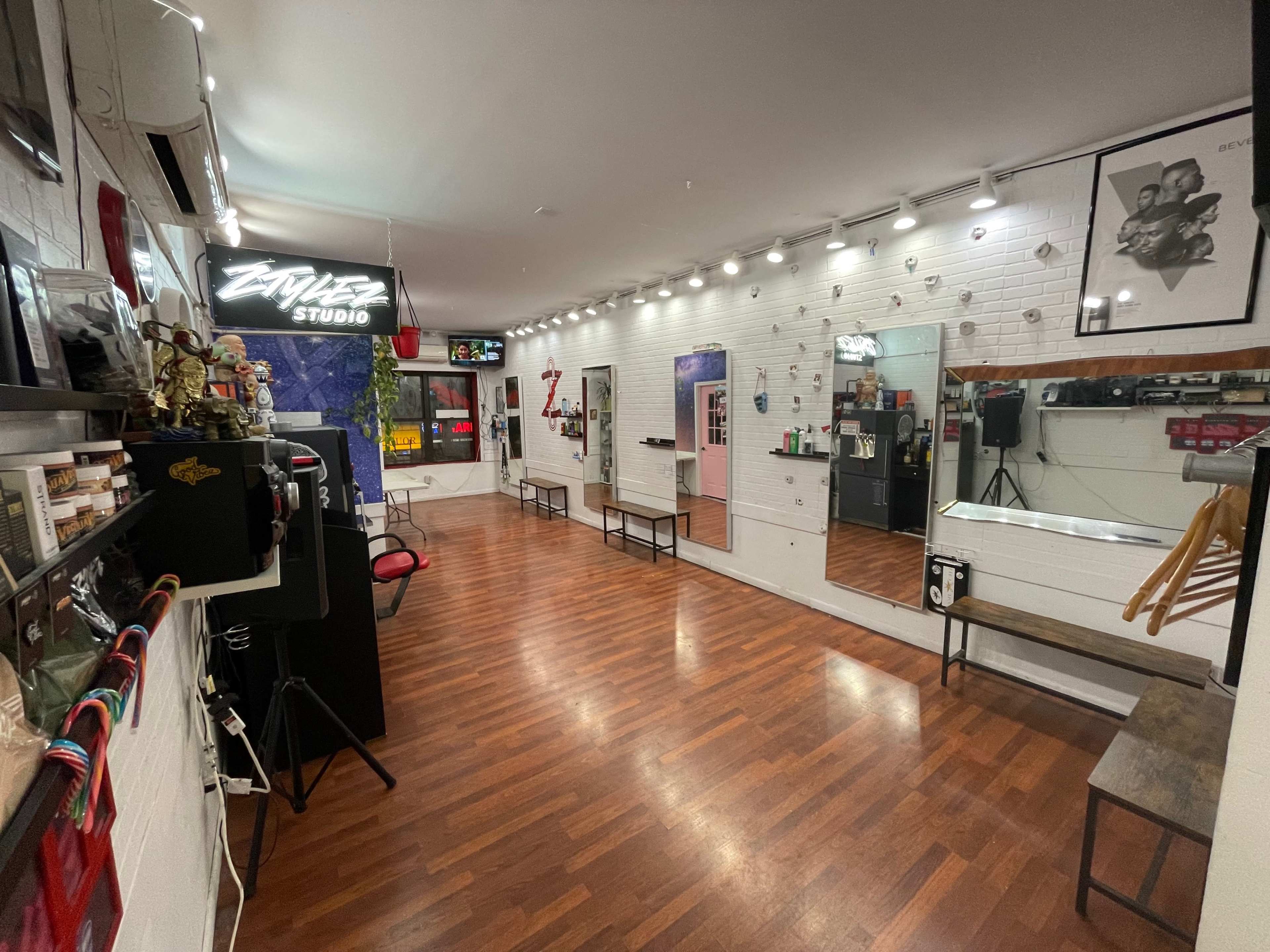 The image shows a well-lit hair studio with wooden flooring, mirrors, and various styling equipment arranged neatly along the walls.