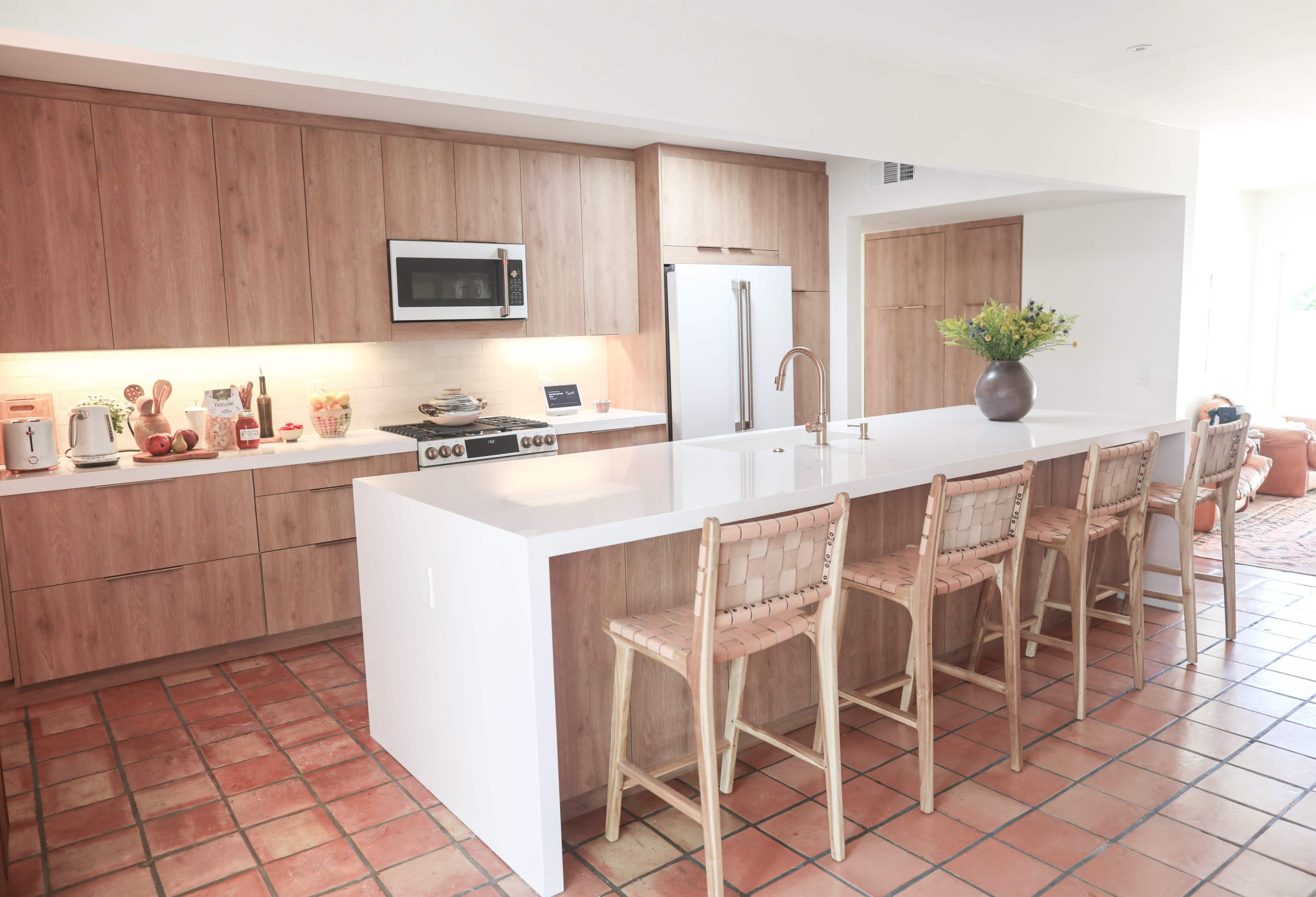 A modern kitchen features wood cabinetry, a central island with bar seating, and stainless steel appliances.