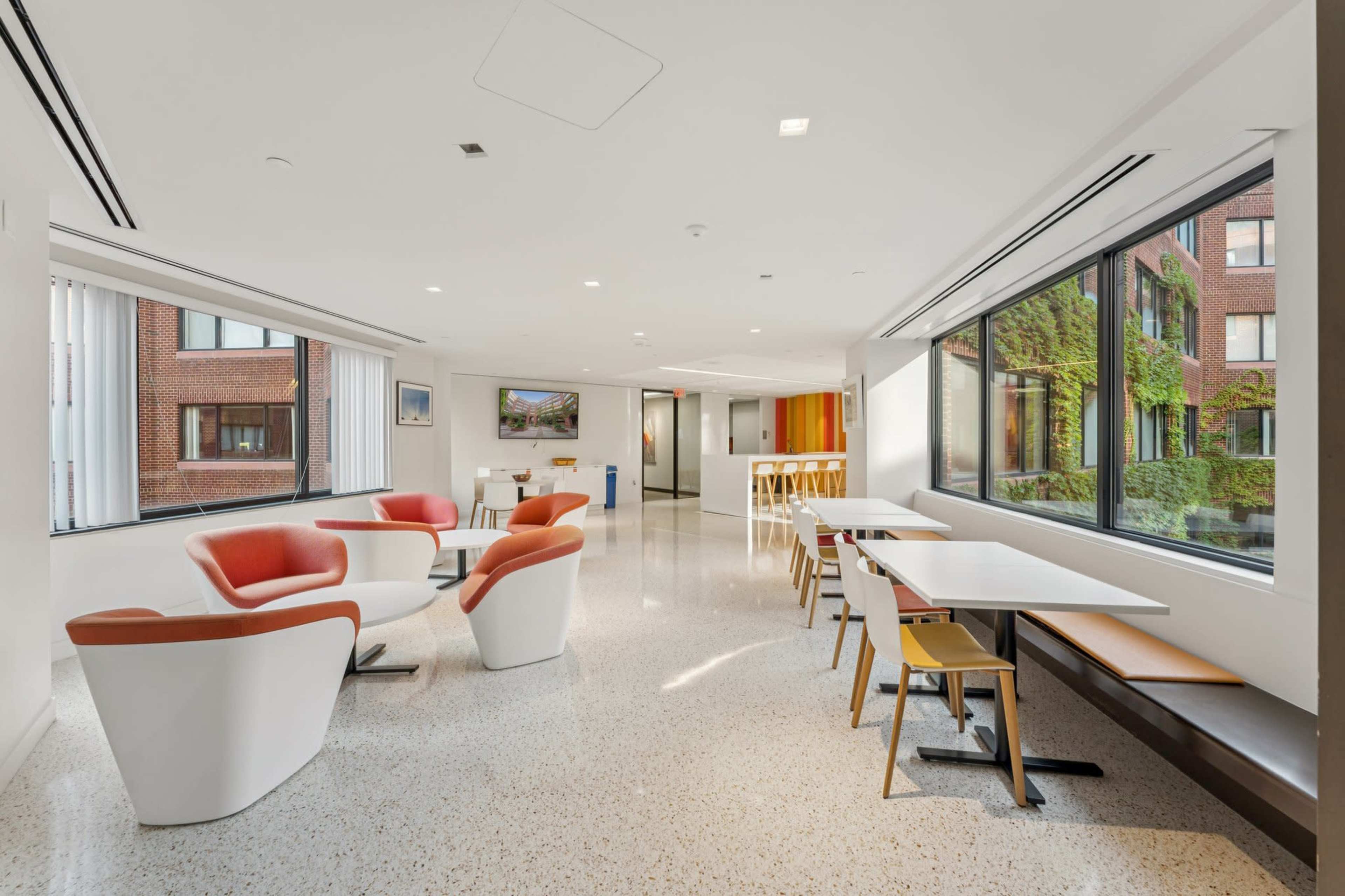 The image shows a modern, bright lounge area featuring comfortable seating and large windows overlooking an outdoor space.