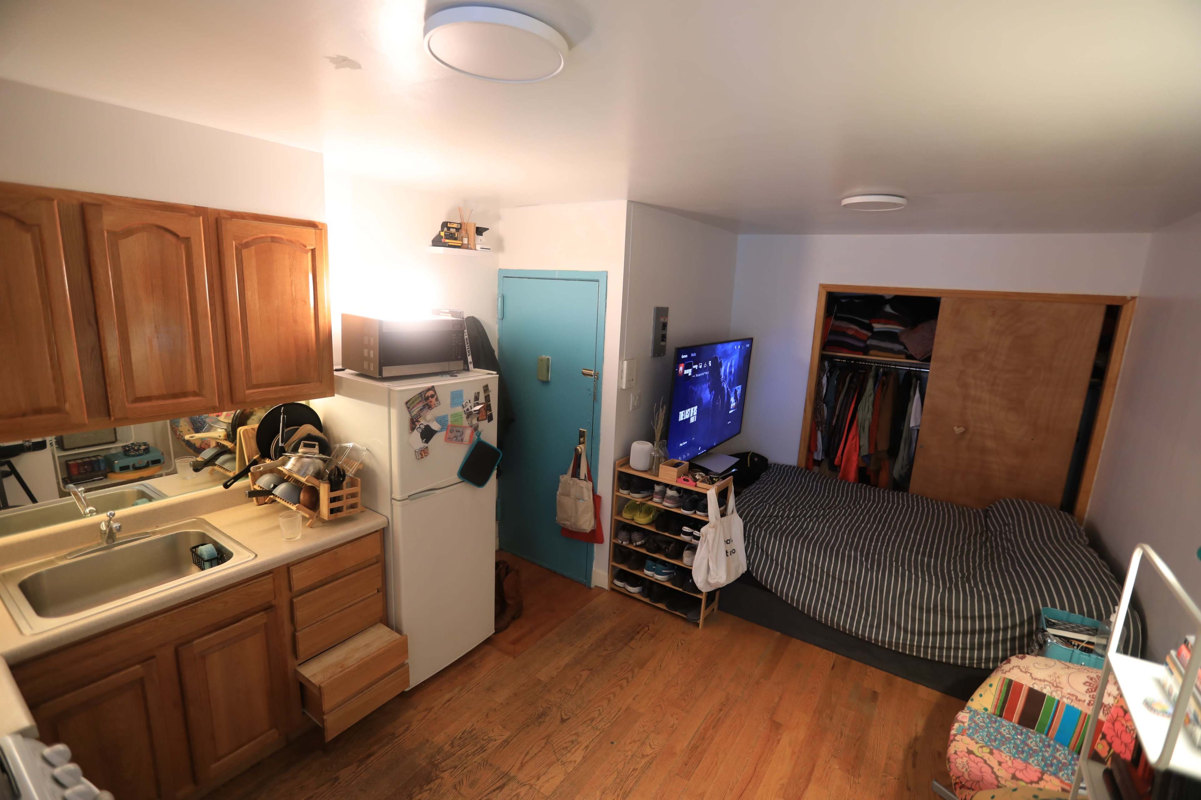 A small studio apartment with a kitchenette, a bed against the wall, and a television mounted on the opposite wall.