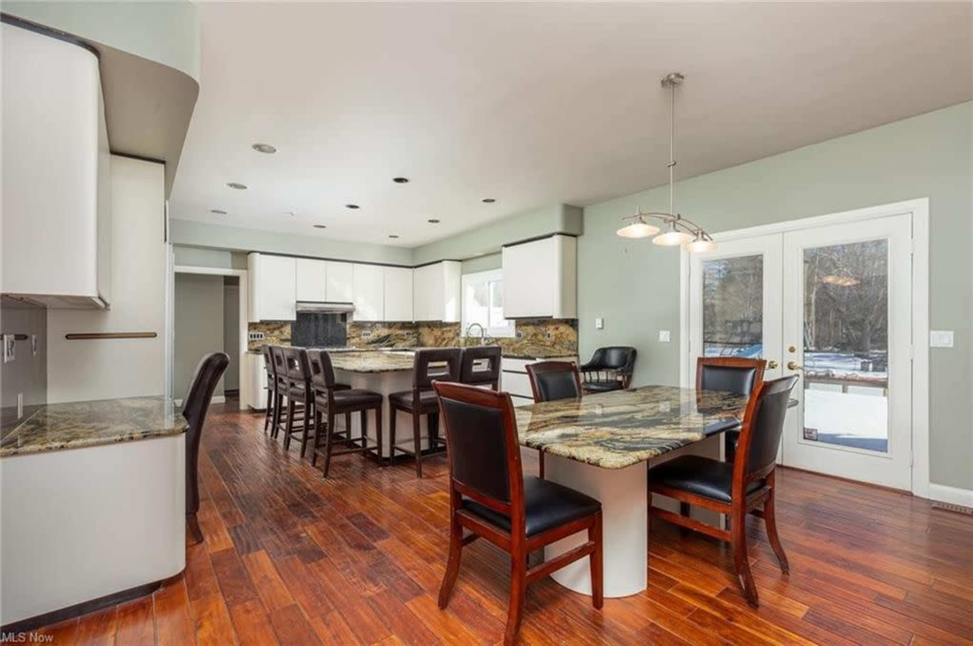 A modern kitchen with dark wood flooring, granite countertops, white cabinets, and a dining table surrounded by black chairs.