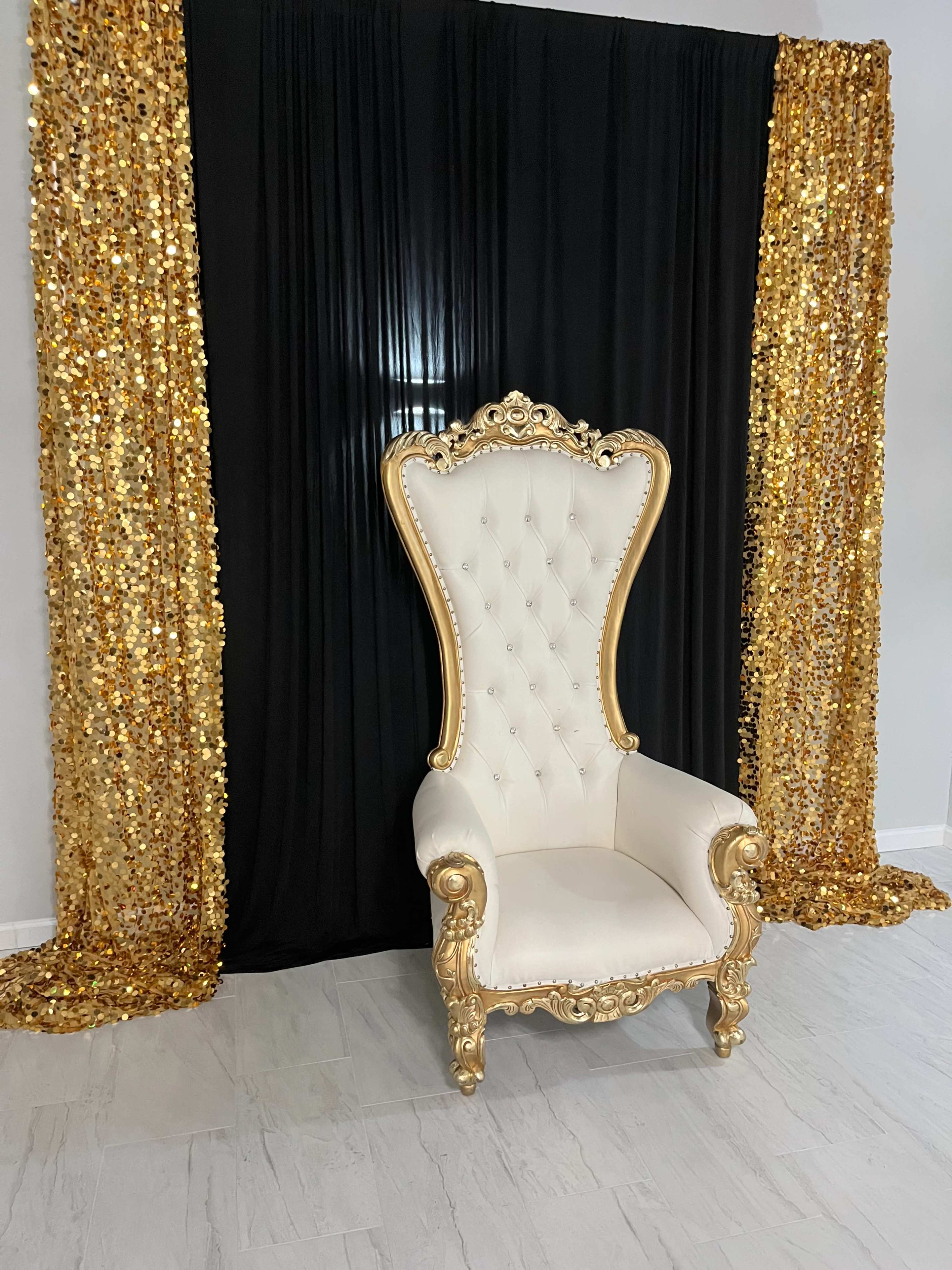 A lavish golden and white throne is positioned in front of a backdrop of black and sparkling gold sequin curtains.
