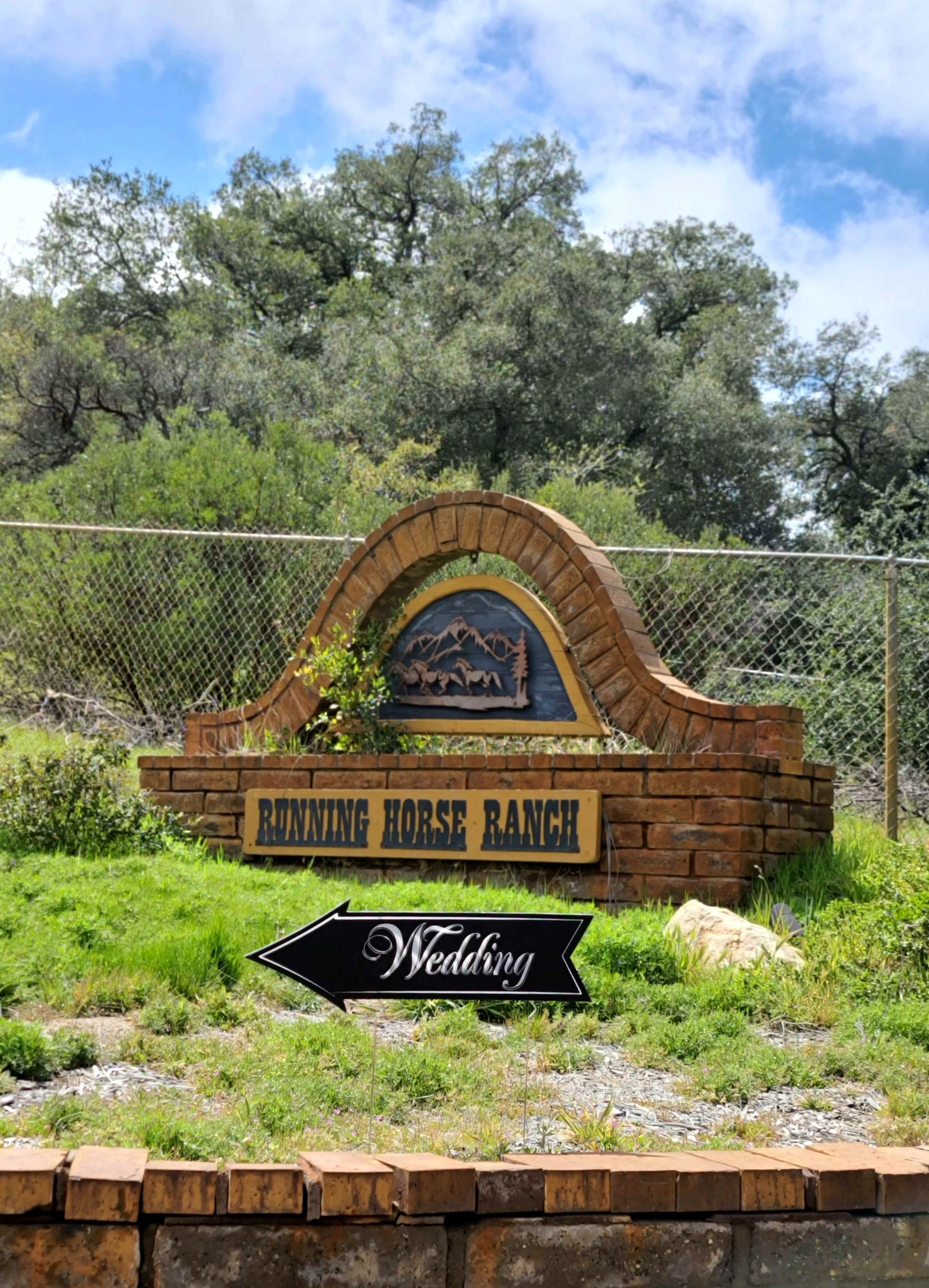 A stone sign for Running Horse Ranch with a directional arrow indicating a wedding event.