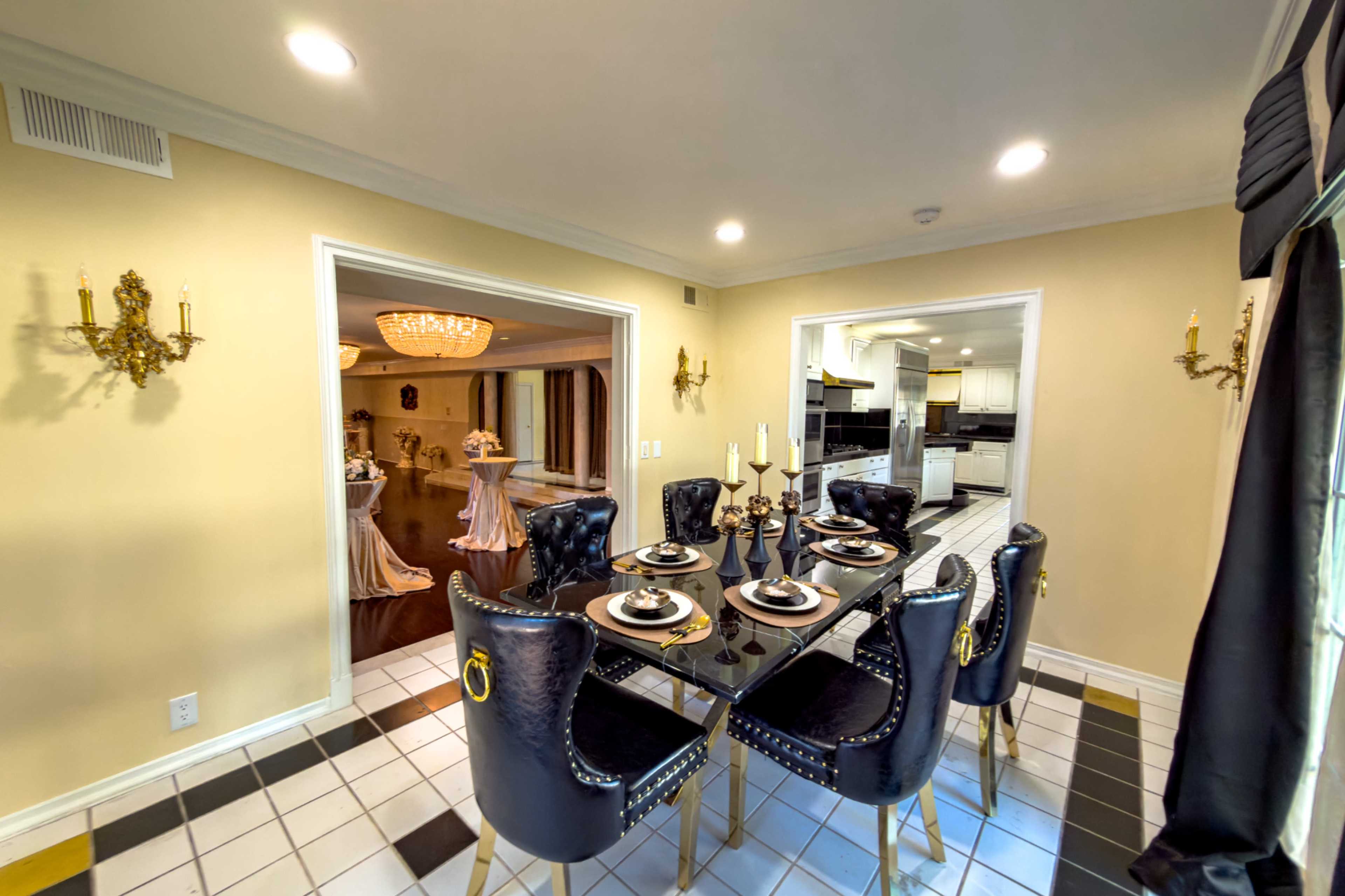 A dining area with a black table and chairs features elegant table settings, leading into a well-lit kitchen area.