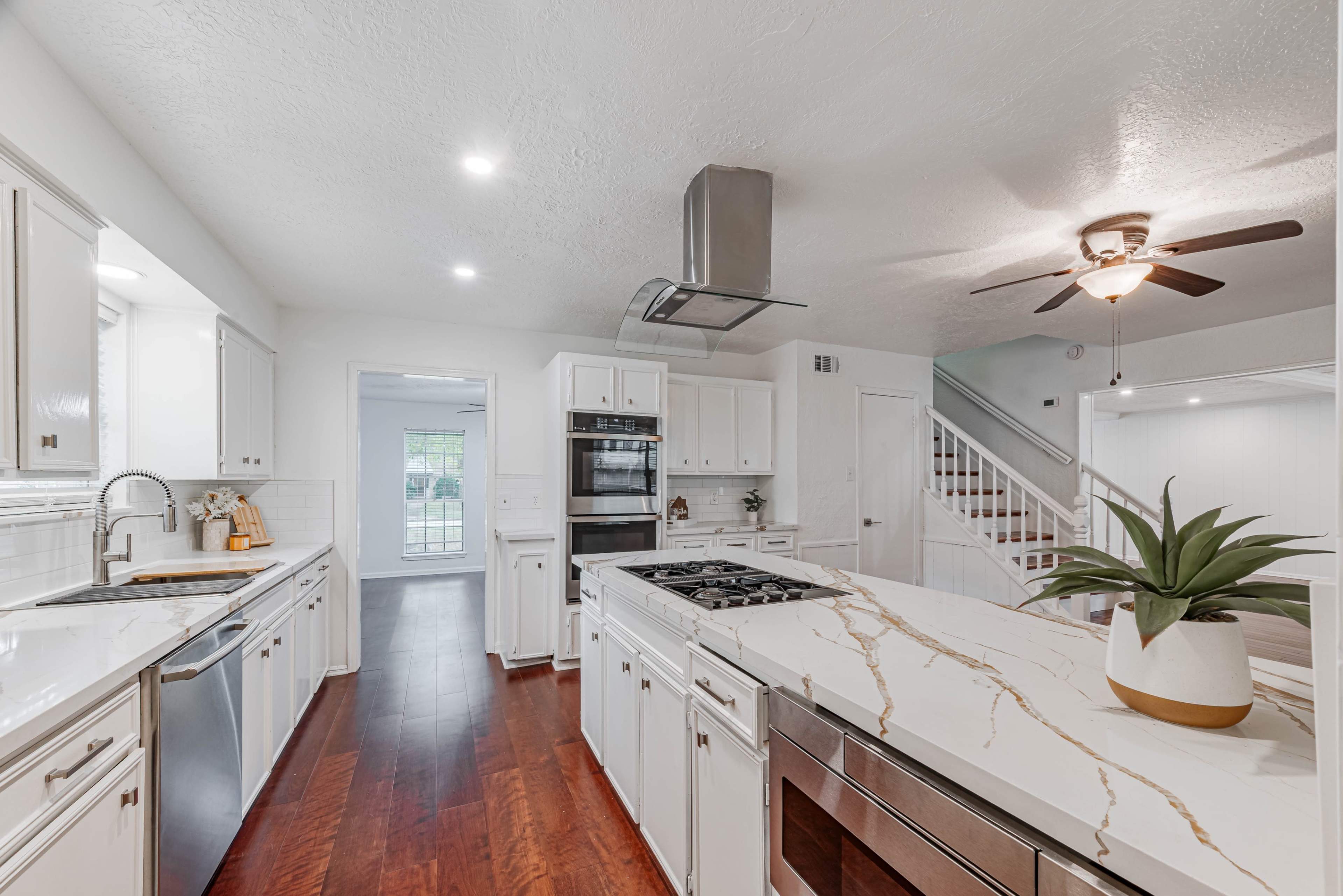 A modern kitchen features white cabinetry, a large marble island with a built-in gas stovetop, stainless steel appliances, and a ceiling fan.