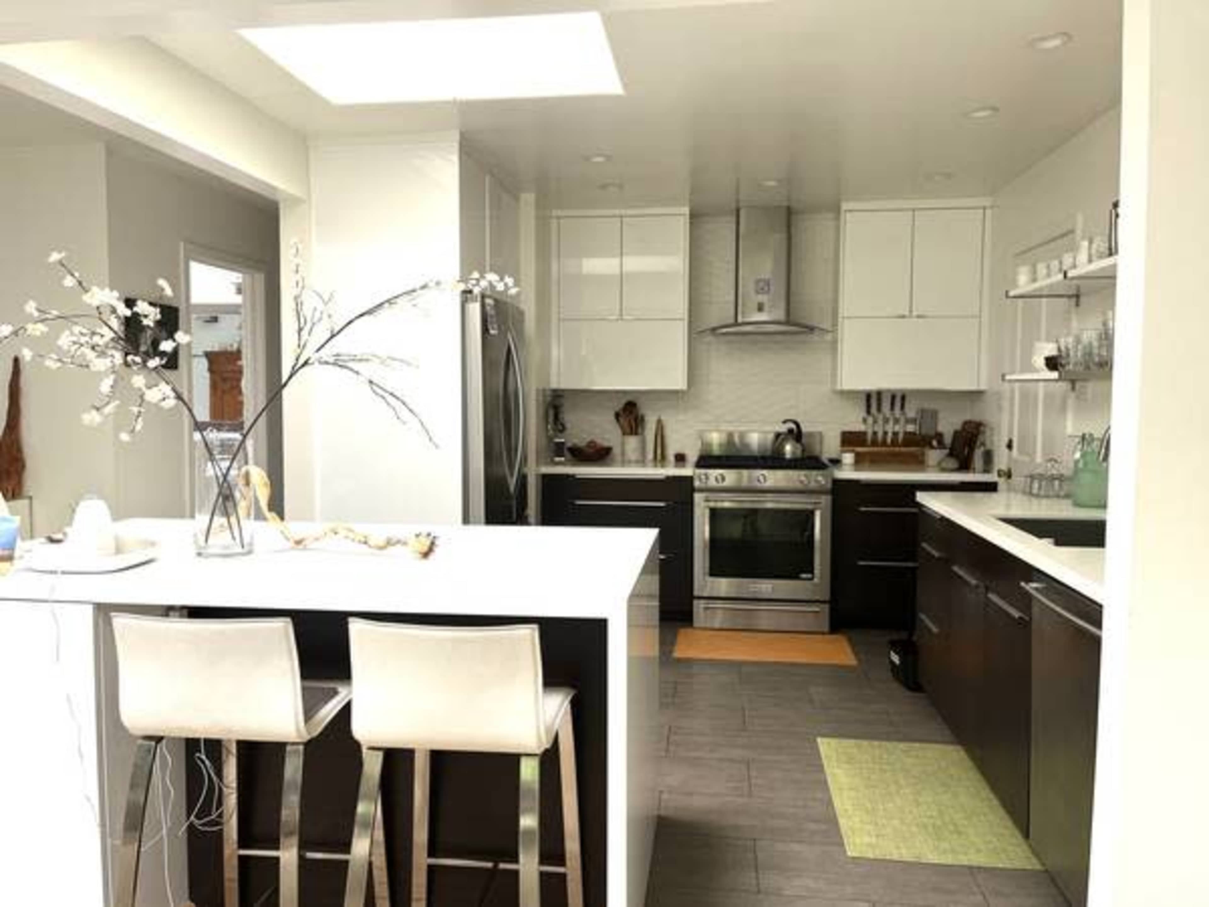 A modern kitchen with sleek cabinetry, stainless steel appliances, and an island with two bar stools.