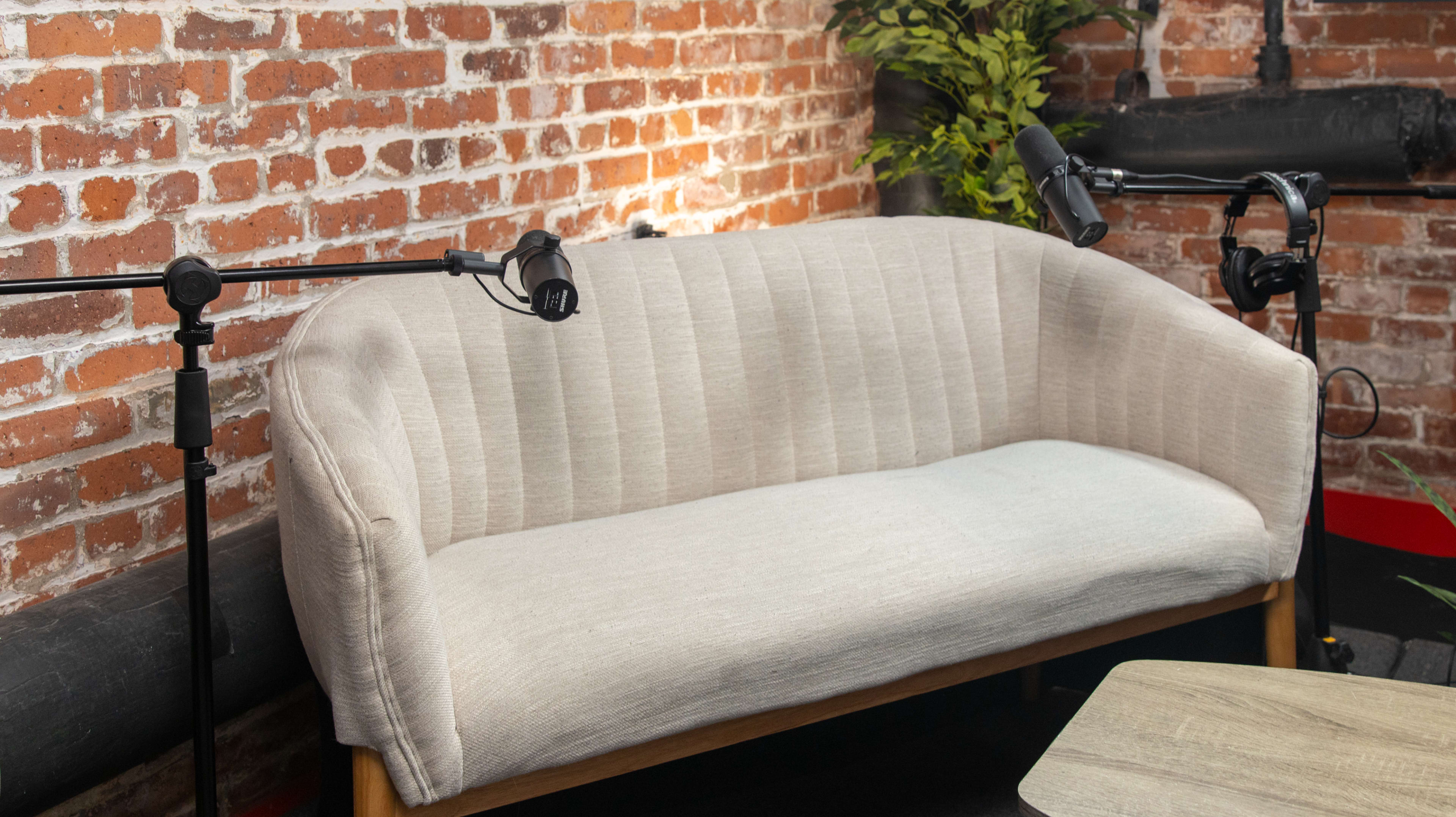 A light-colored sofa is positioned against a brick wall, with two microphones mounted on stands nearby.