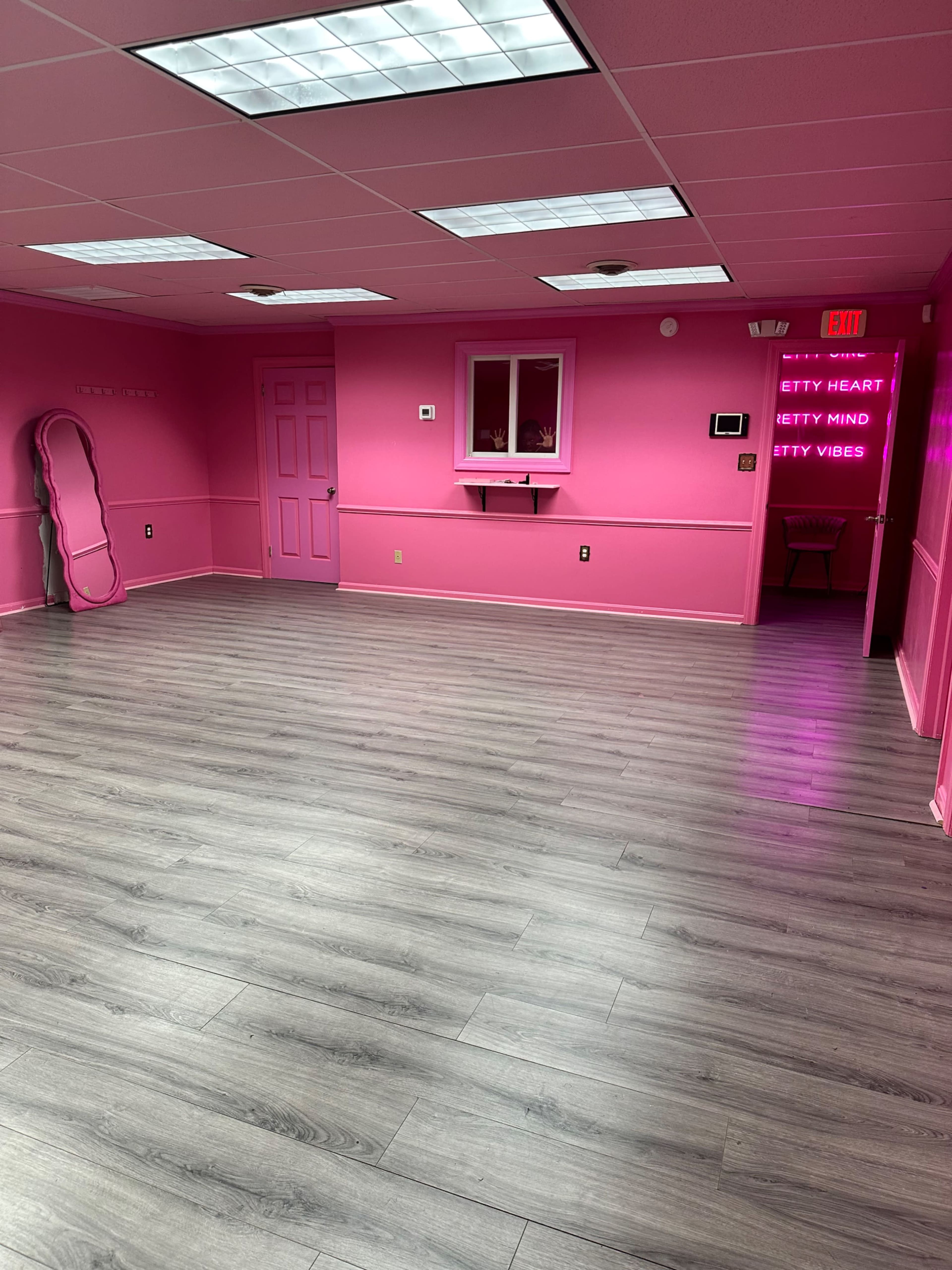 The room features bright pink walls and a gray wooden floor, with a mirror and door visible on one side.