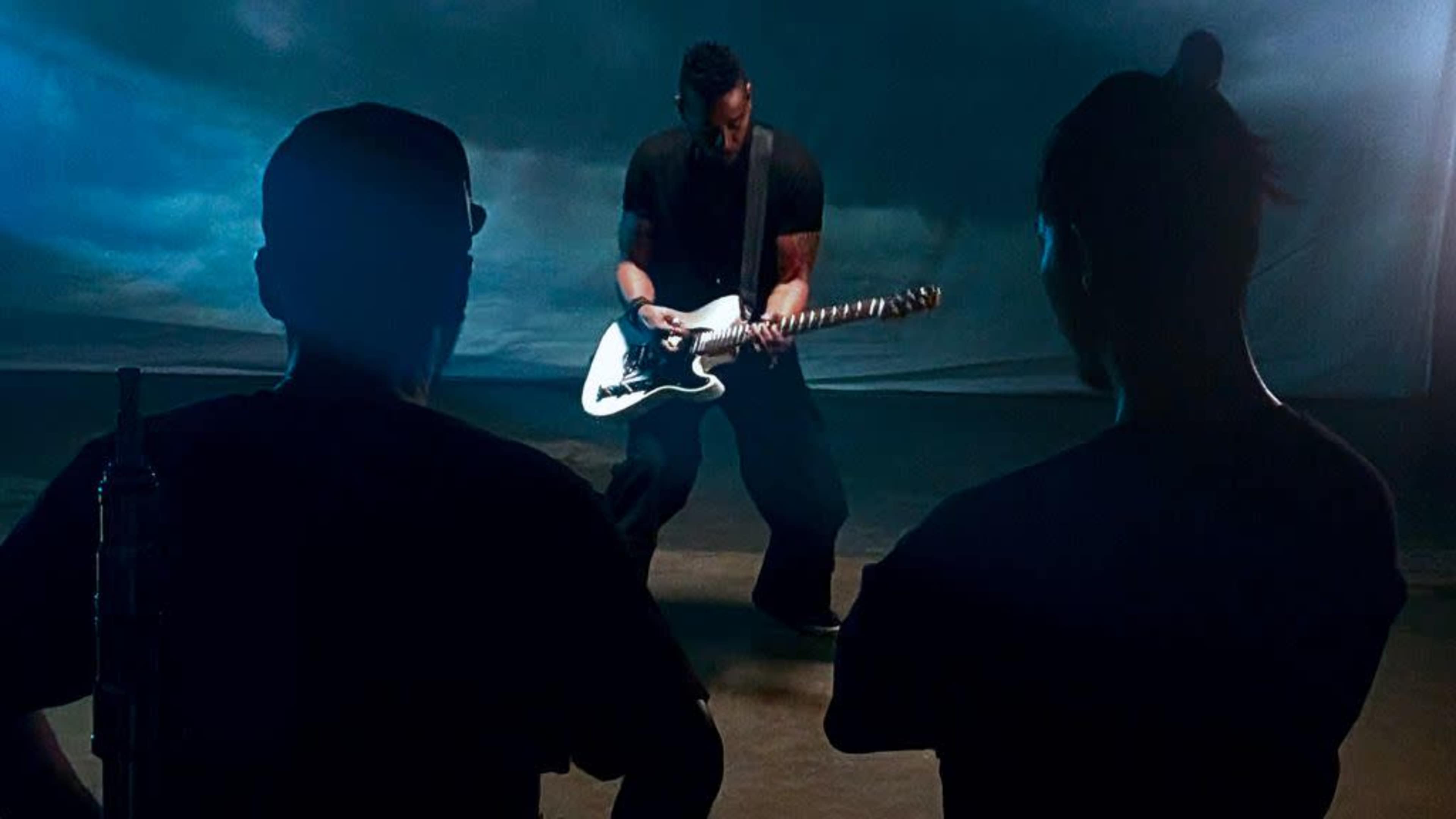 A guitarist performs on stage while two audience members watch from the foreground.