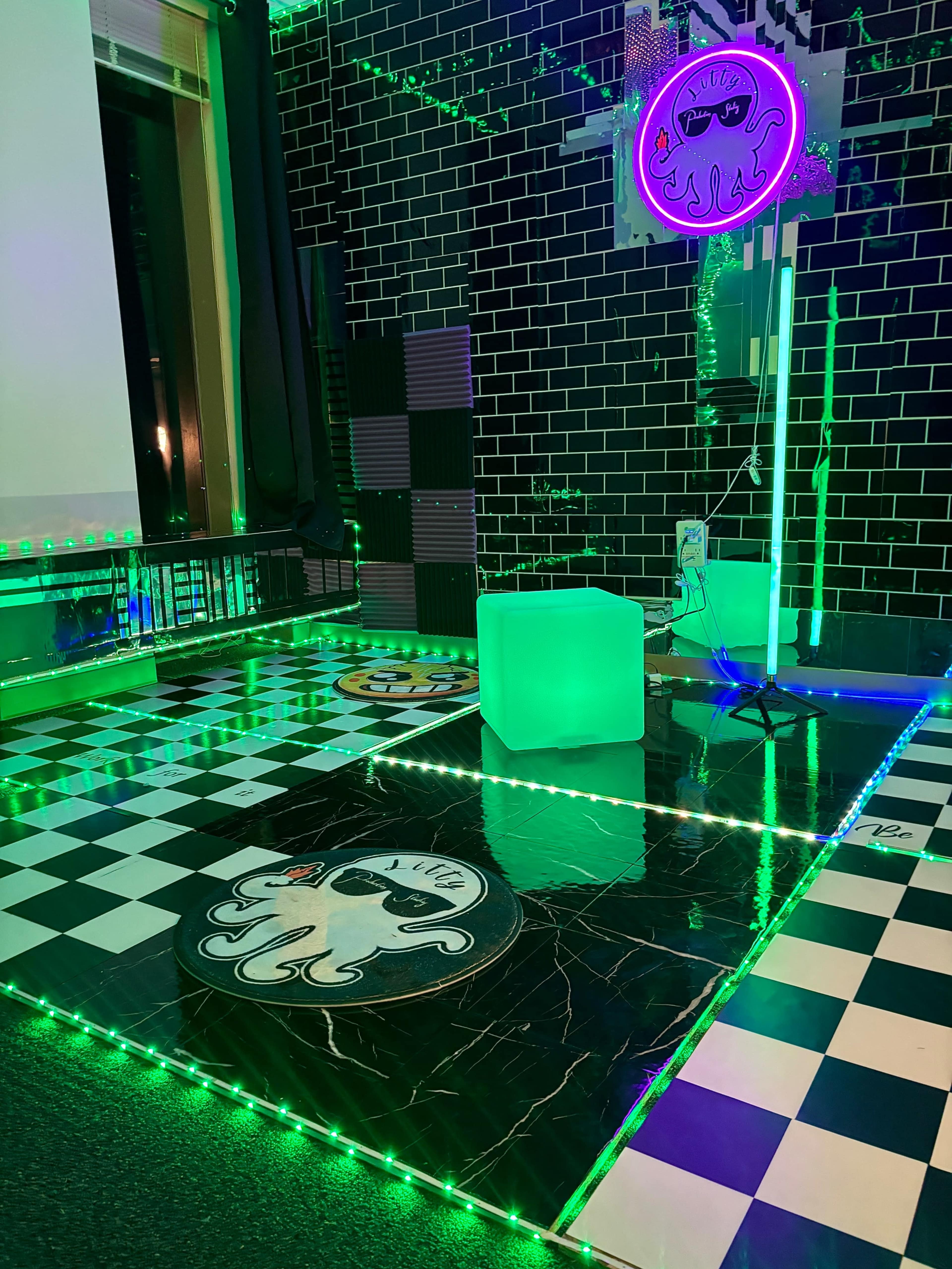 The image features a room with a checkered black and white floor, glowing green LED lights, and decorations including an octopus design on the floor and a neon octopus lamp.