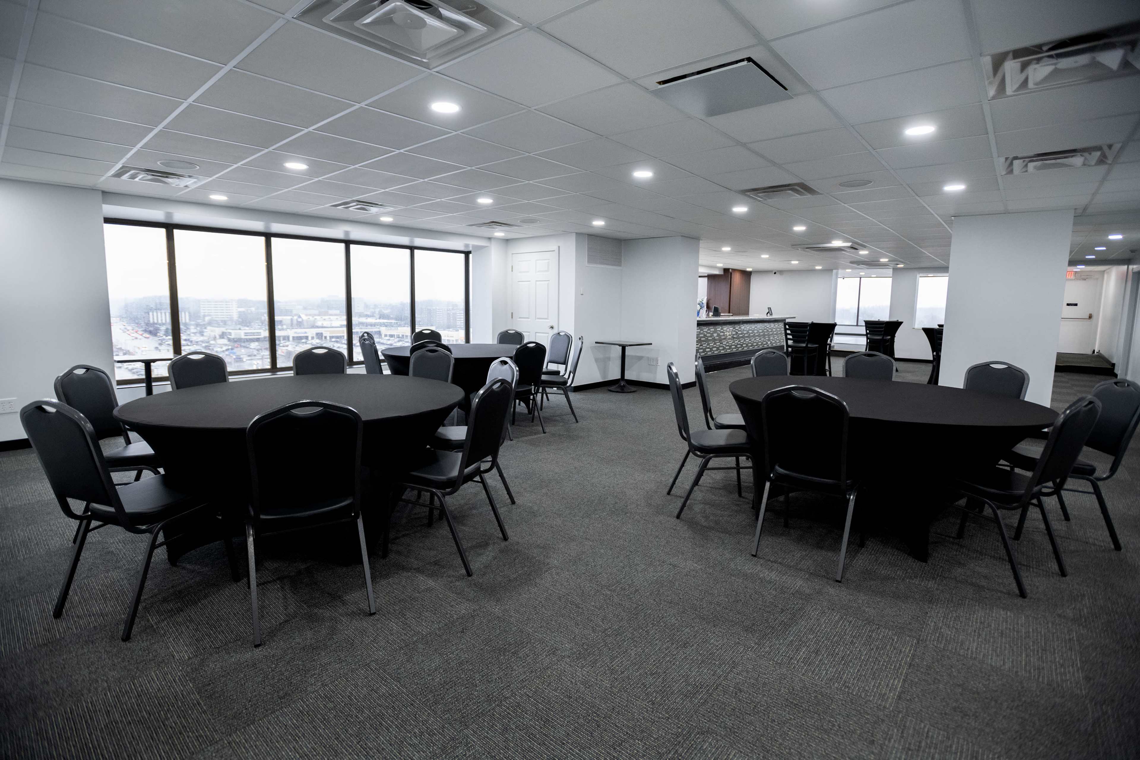 A conference room features several circular black tables arranged in a spacious, well-lit area with large windows.
