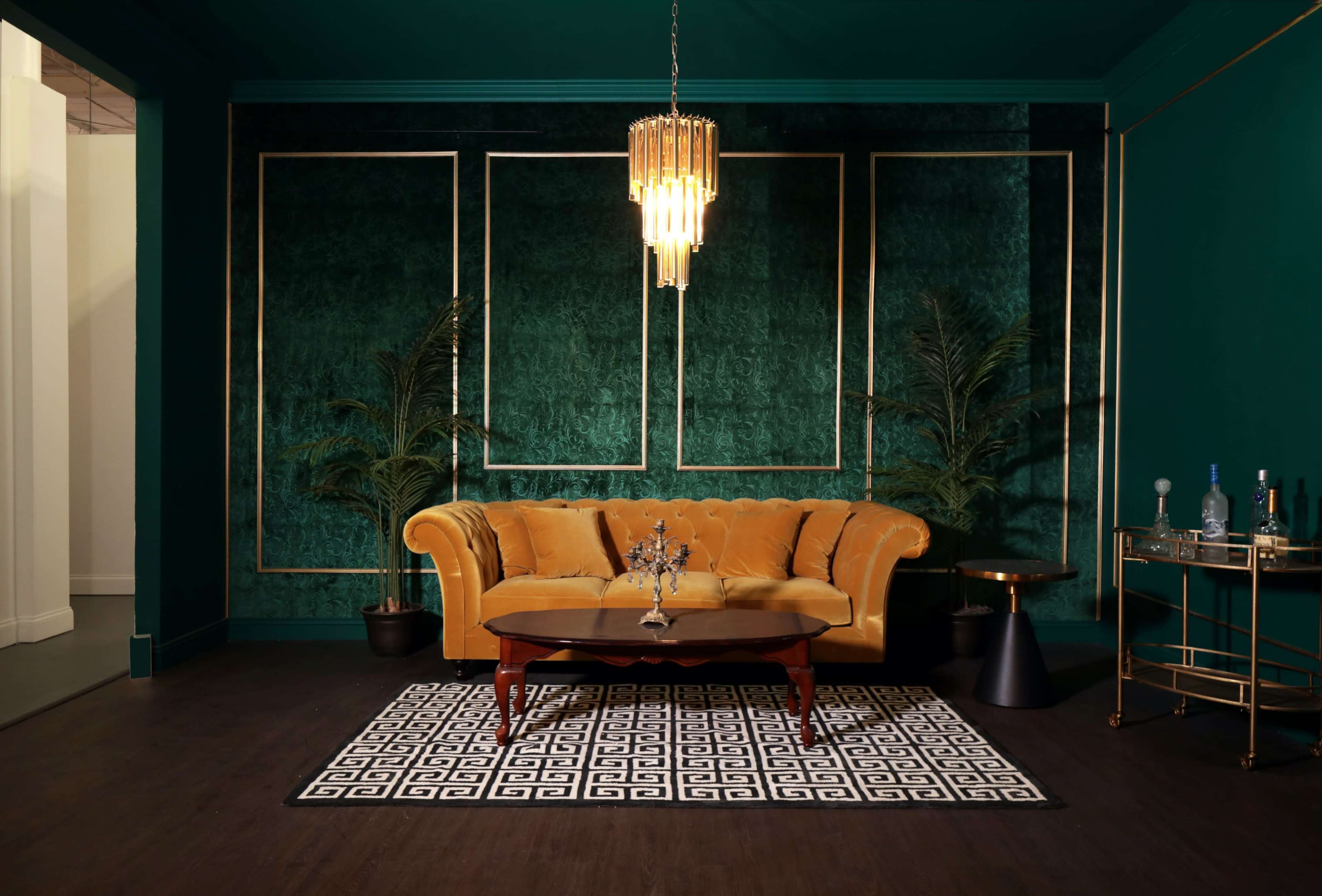 A mustard-colored sofa is placed in front of a dark green wall with gold accents, accompanied by a round table and decor items.