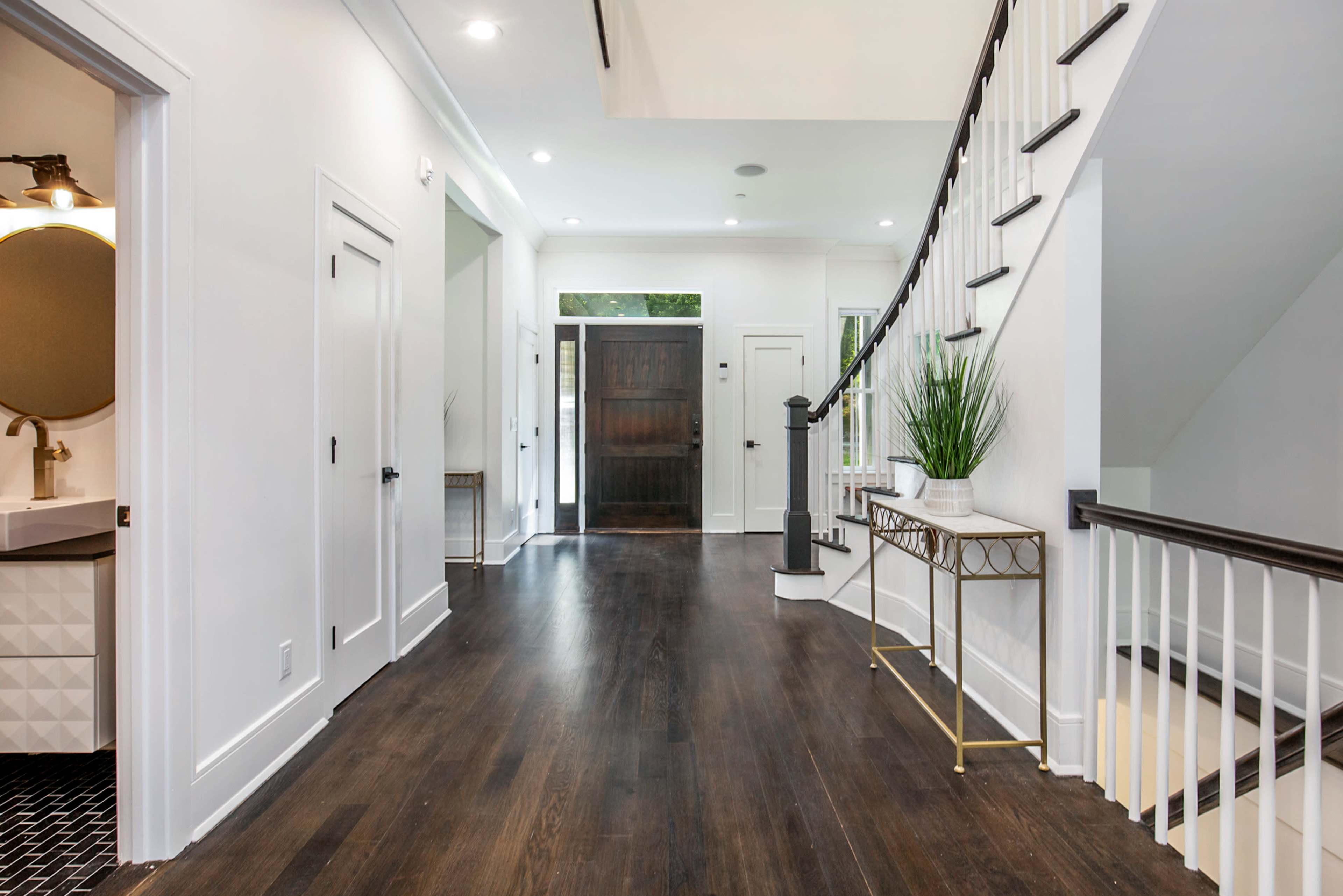 A bright, modern foyer with hardwood floors, a staircase, and a decorative console table against a wall.
