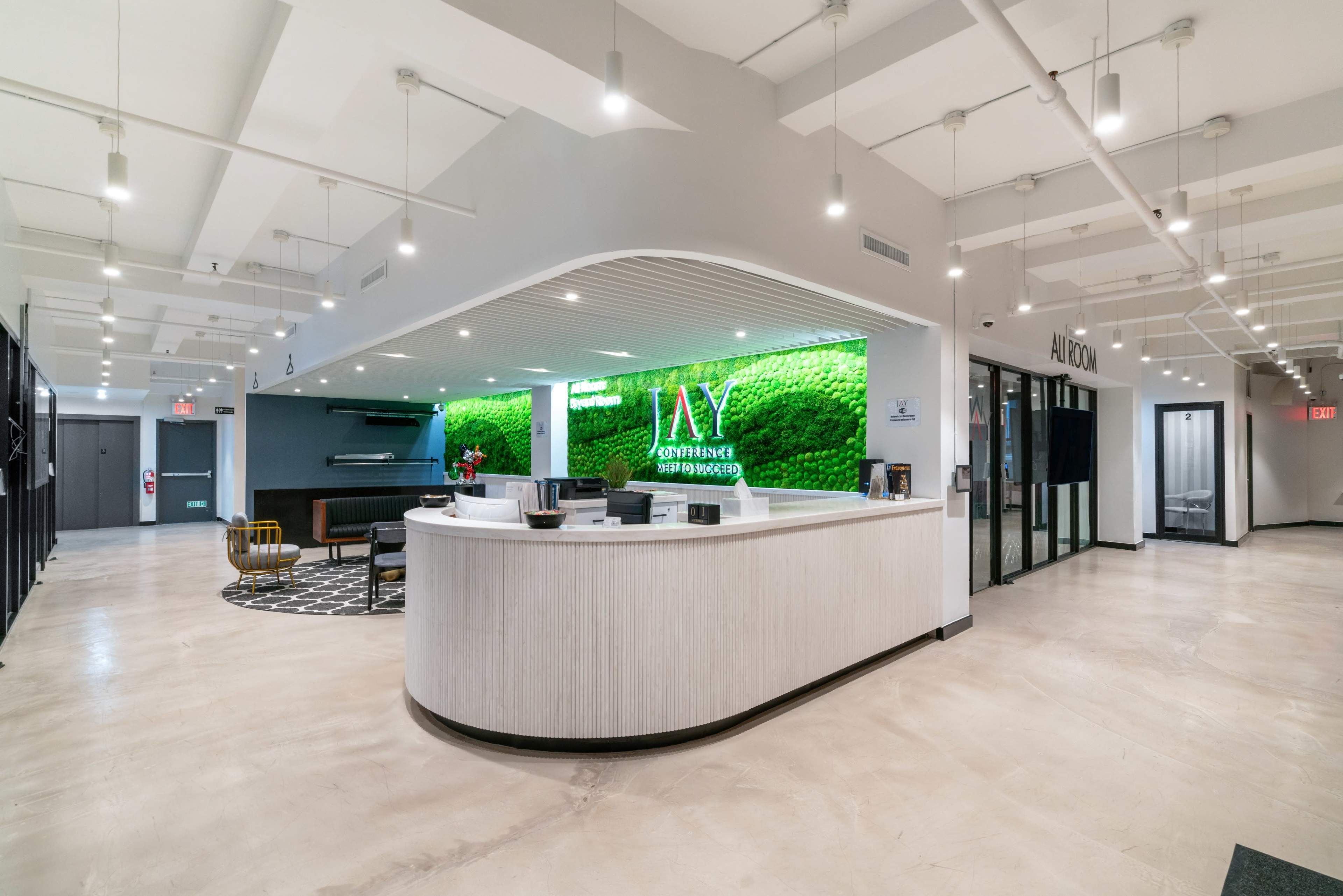 The image shows a modern reception area featuring a curved white front desk, green moss wall art, and a spacious, well-lit interior design.