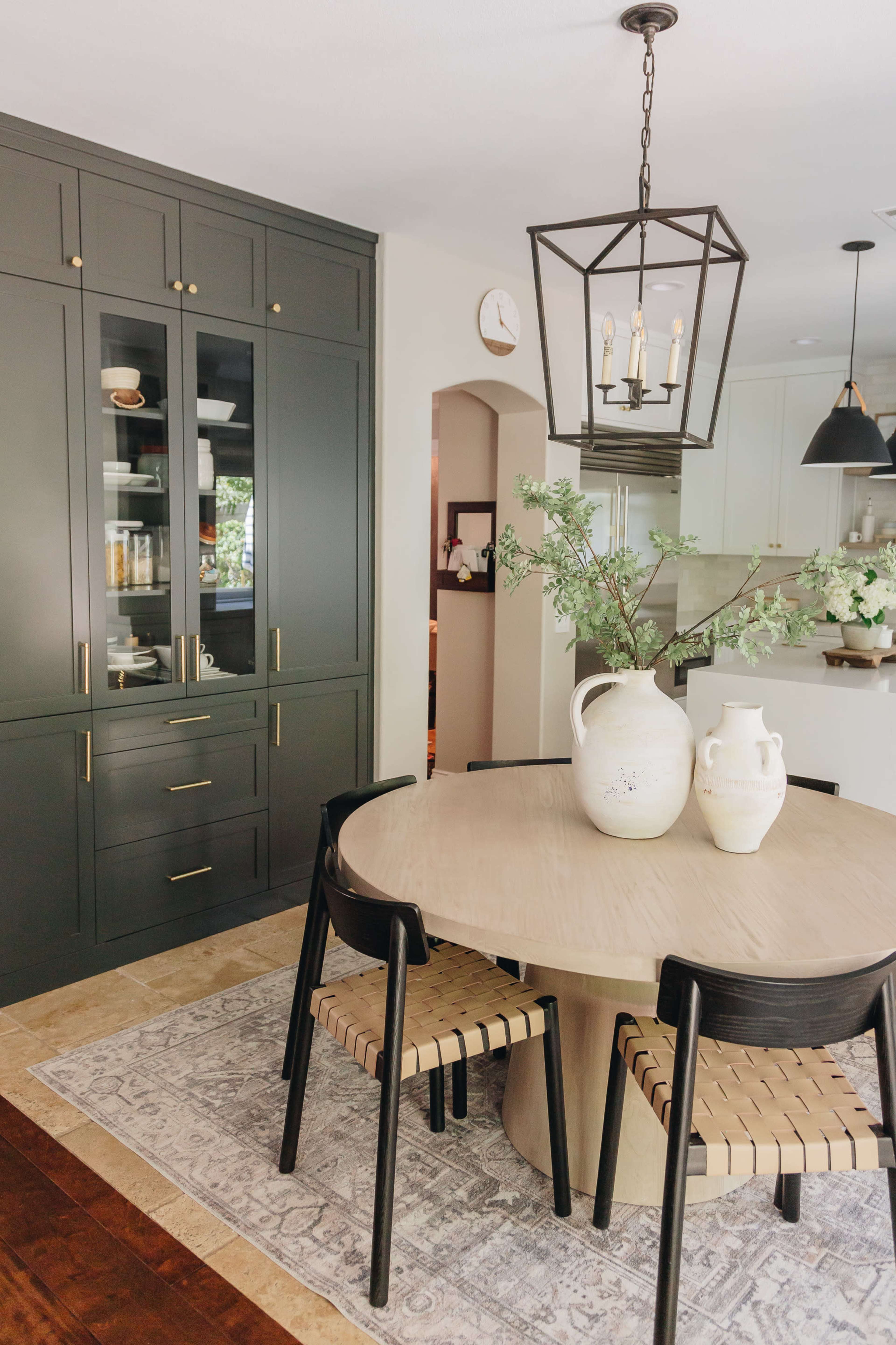 A modern dining area with a round table surrounded by black chairs and a cabinet with glass doors, featuring a lantern-style light fixture above.