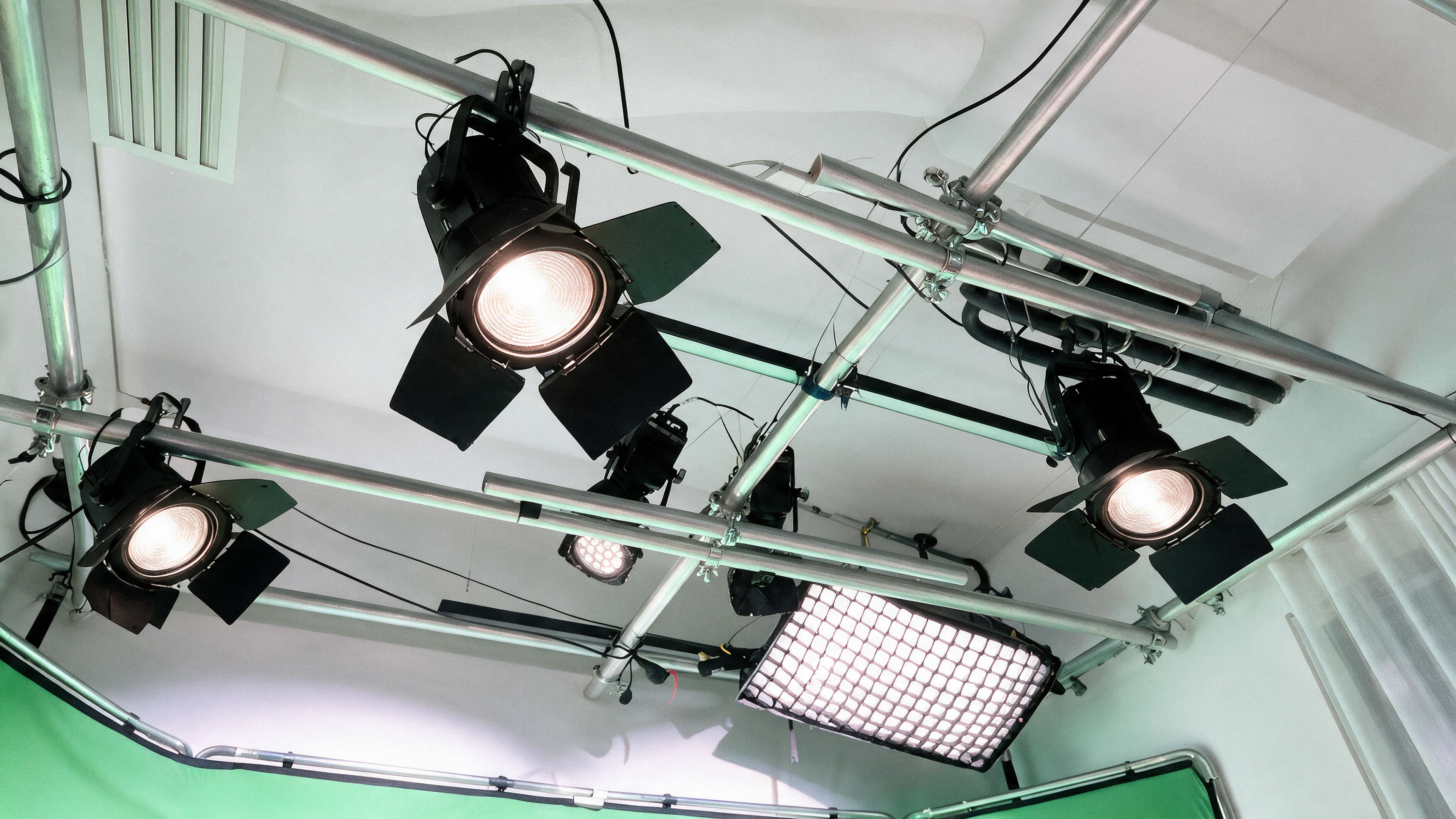 The image shows a setup of studio lights mounted on metal frames with a green backdrop.