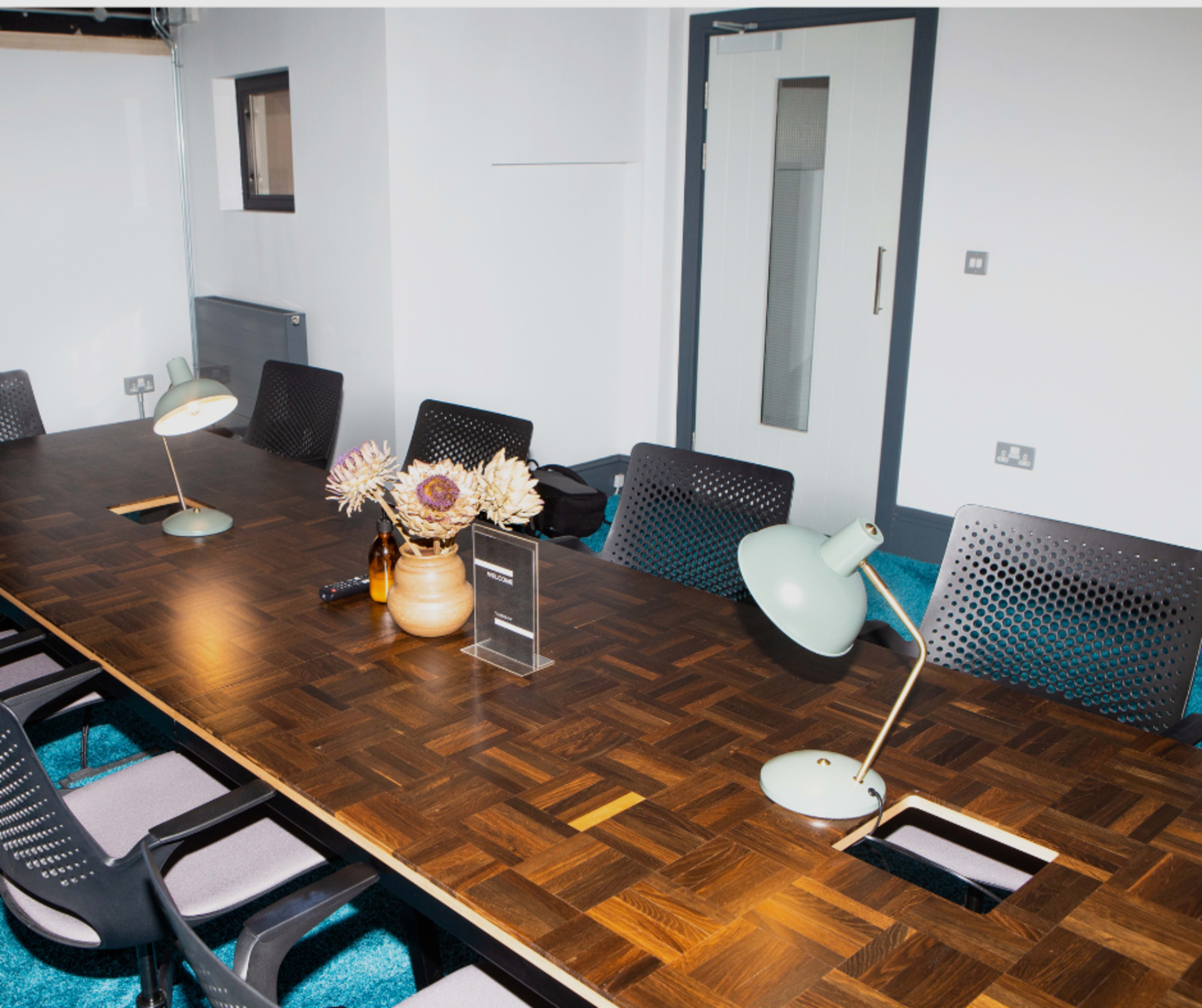 A large wooden conference table is set in a room with modern chairs, lamps, and a decorative vase.