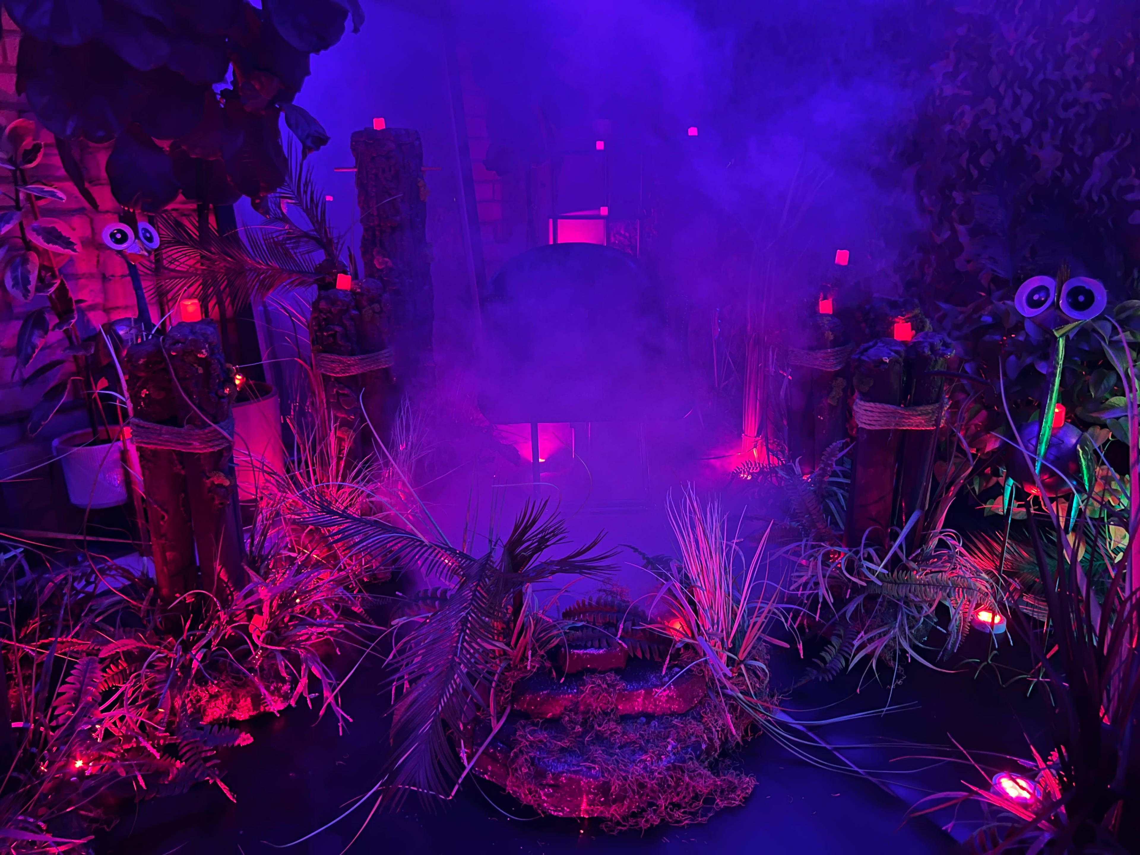 The scene features a vibrant, misty environment adorned with illuminated plants, wooden structures, and colorful lighting effects.