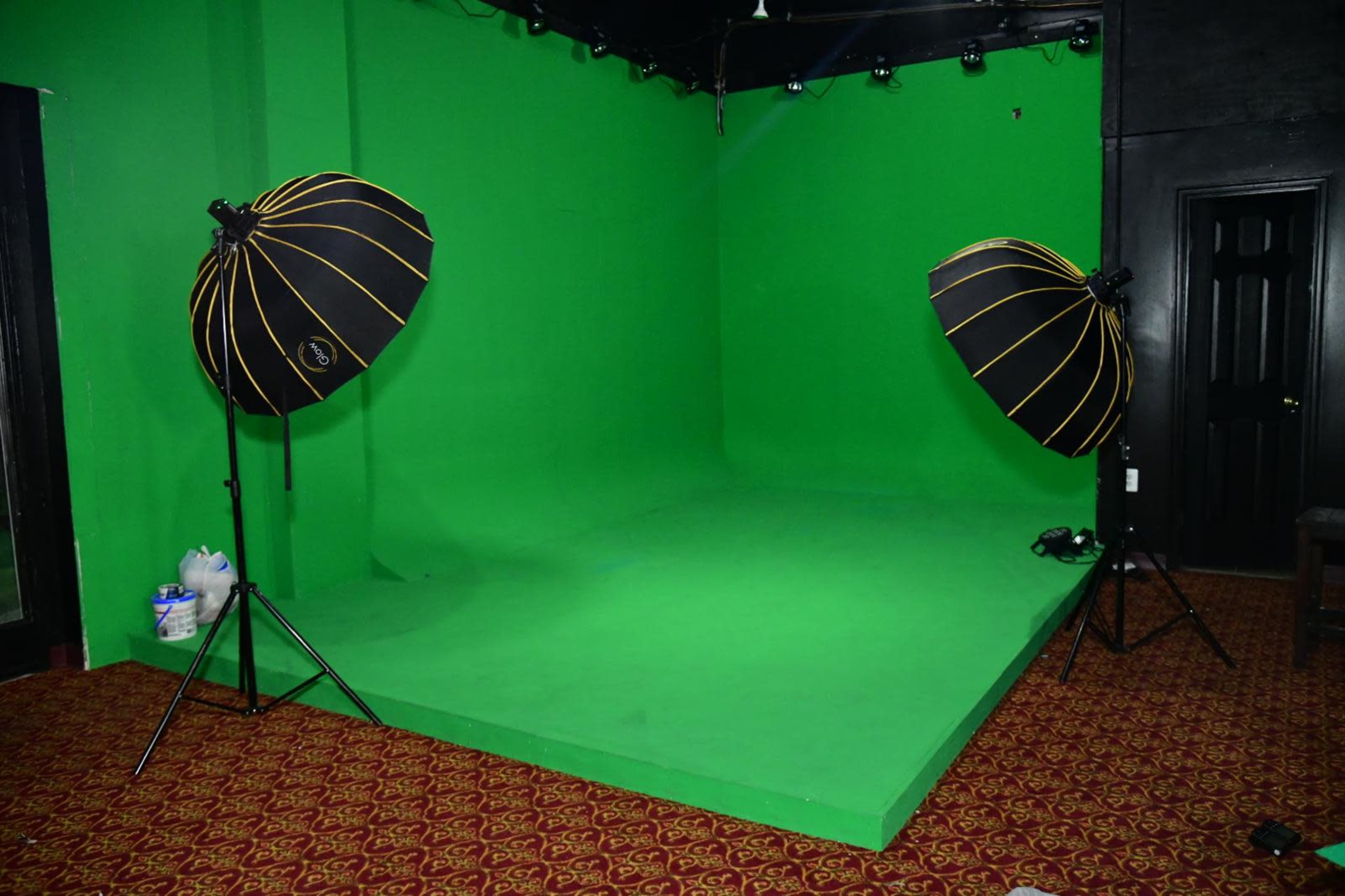 The image shows a green screen studio setup with two large softbox lights positioned on either side of a green backdrop.