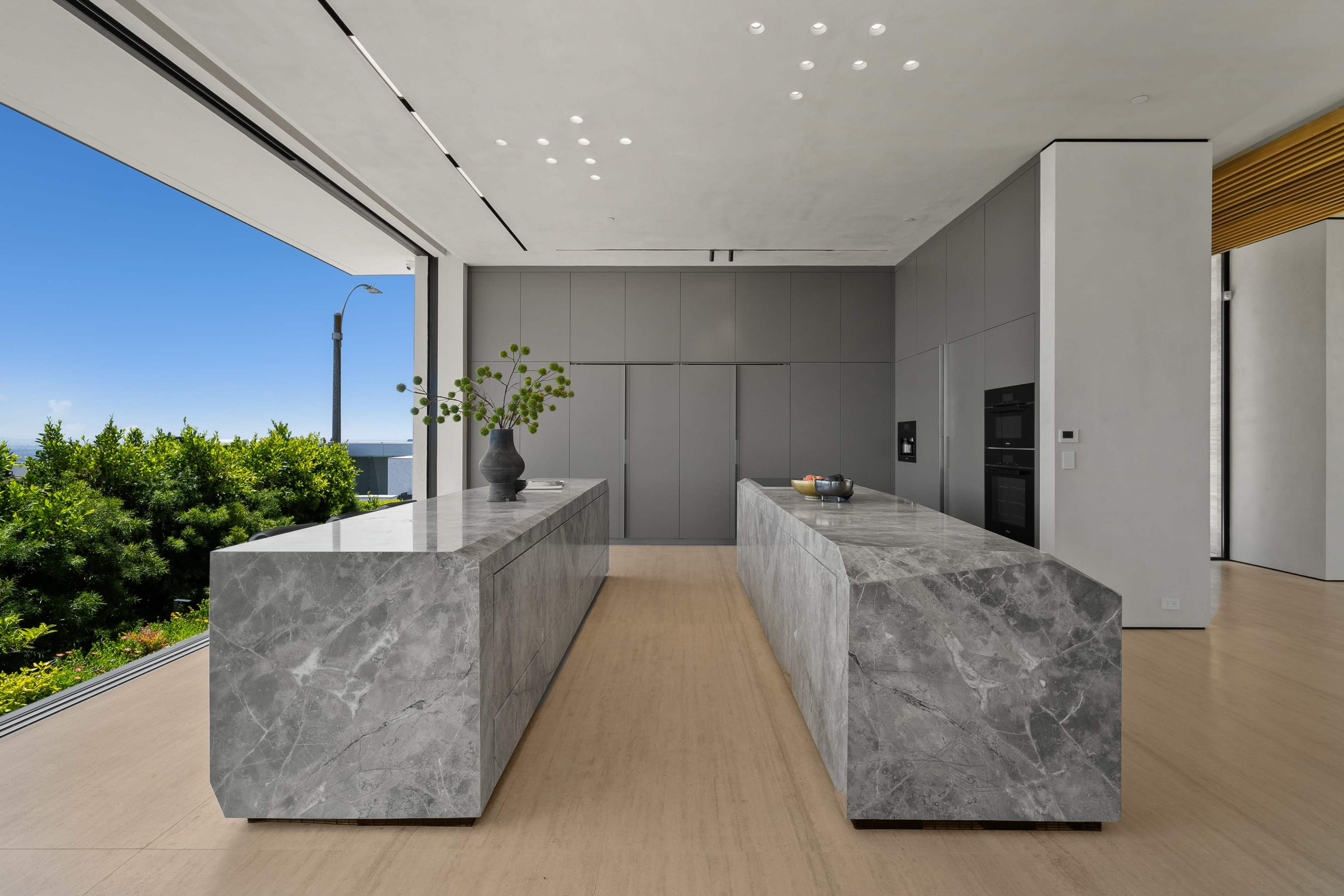 A modern kitchen featuring two large marble countertops with a view of greenery outside.