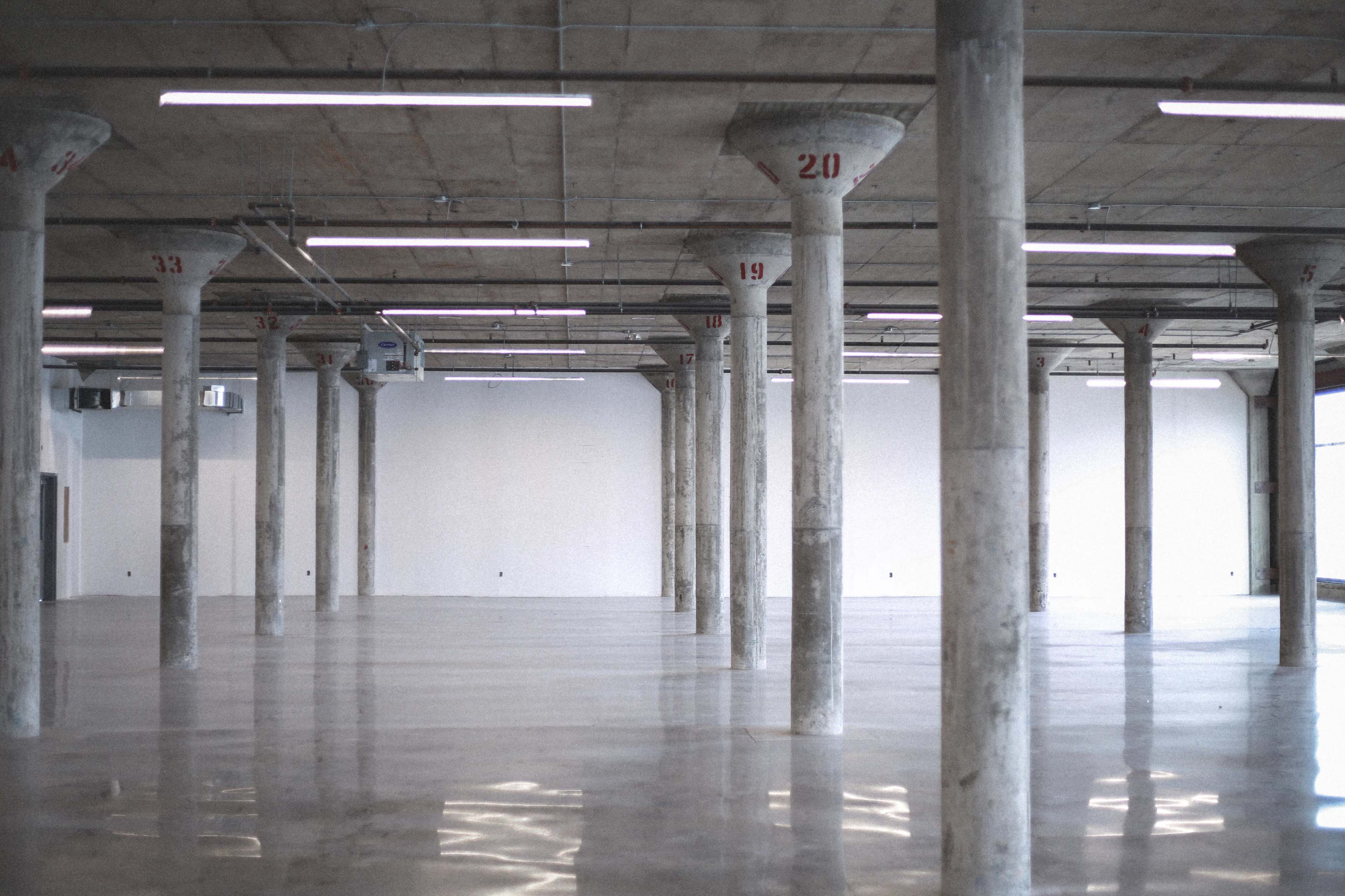 The image shows a spacious, industrial interior with concrete pillars labeled with numbers and a polished floor.