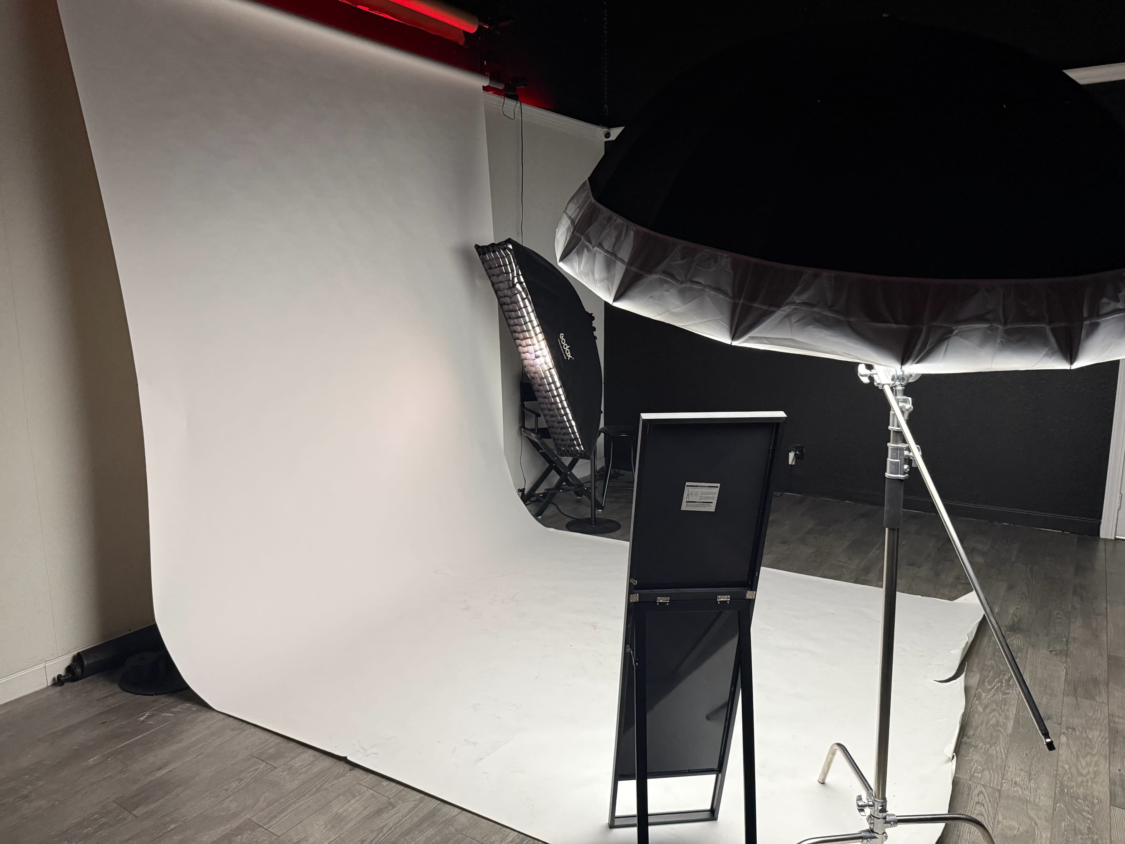 The image shows a photography studio setup featuring a white backdrop, a softbox light, and a mirror on a stand.