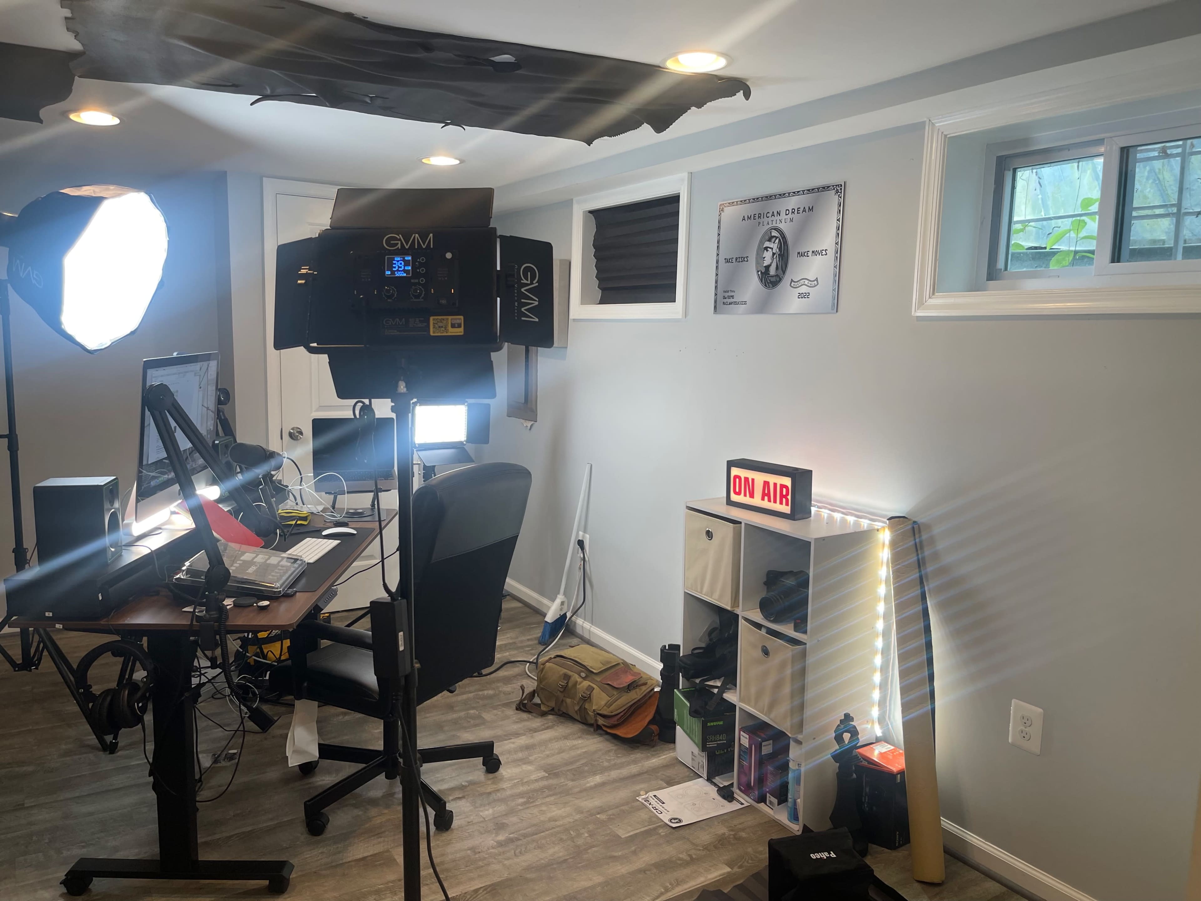 A small office setup featuring a desk with a computer, lighting equipment, and a shelf labeled "ON AIR."