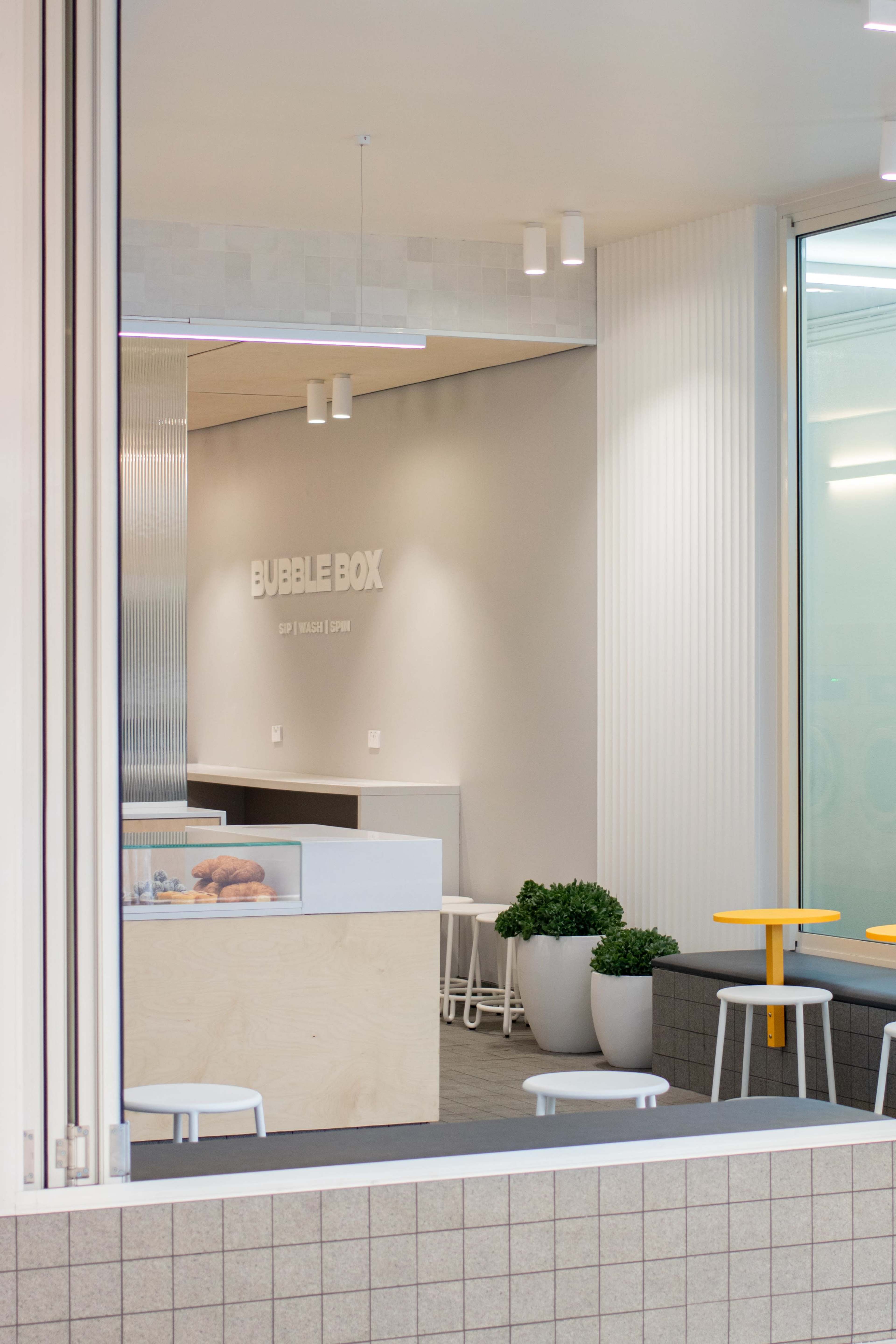 A modern café interior with a minimalist design, featuring light-colored walls, simple furniture, and a sign that reads "BUBBLE BOX."