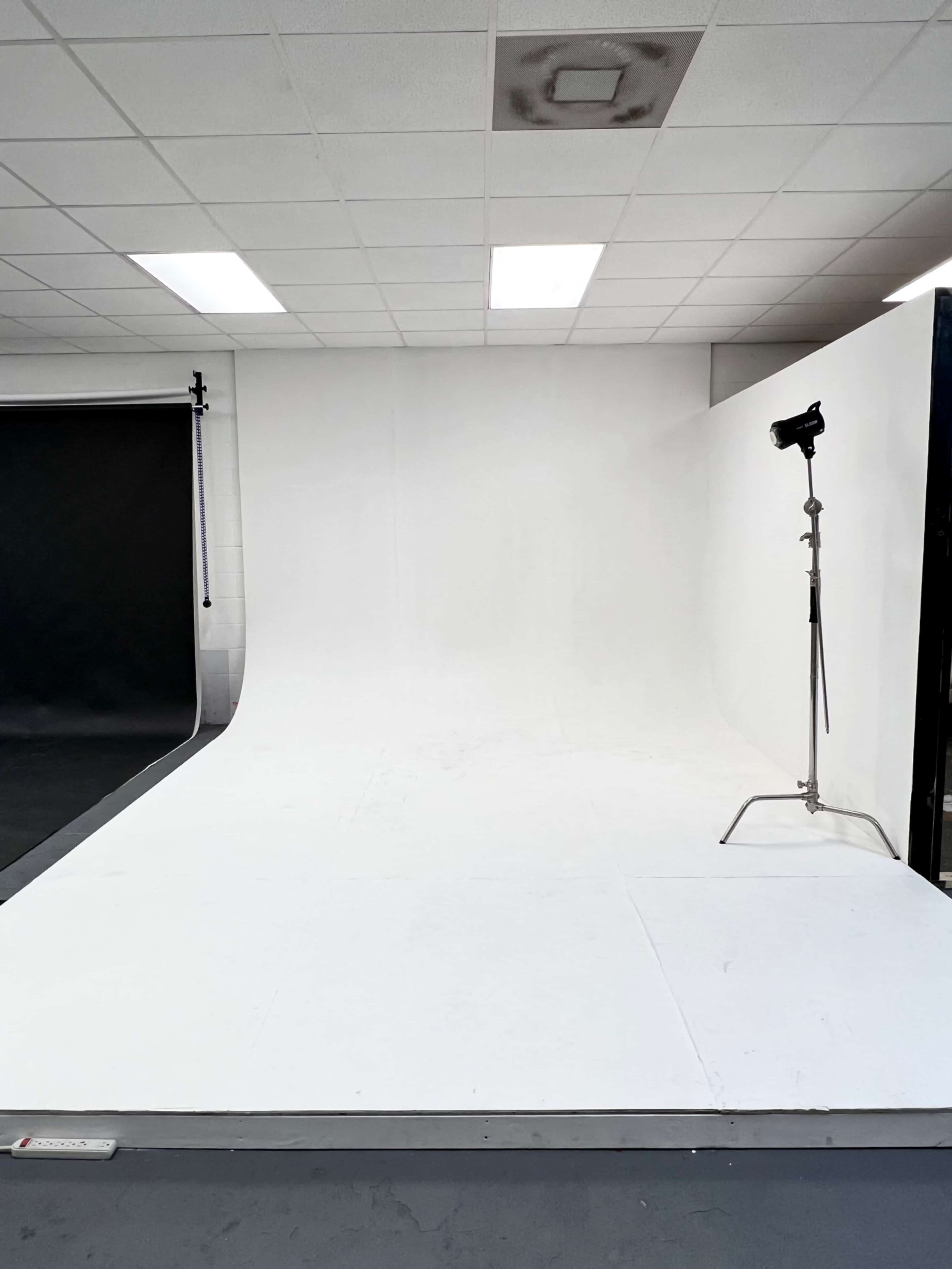 A photography studio with a seamless white backdrop and a floor consisting of white panels, accompanied by a light stand.