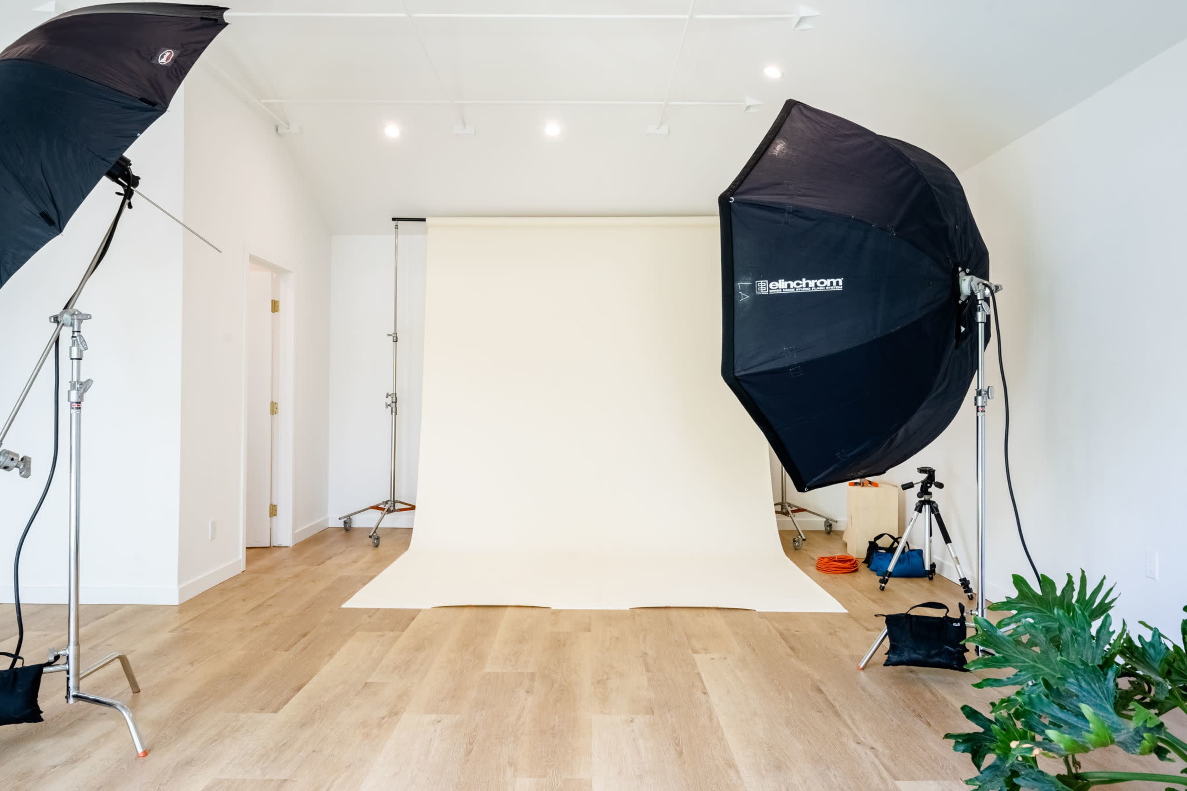 A photography studio with a light-colored backdrop, two adjustable softbox lights, and a camera setup on a tripod.