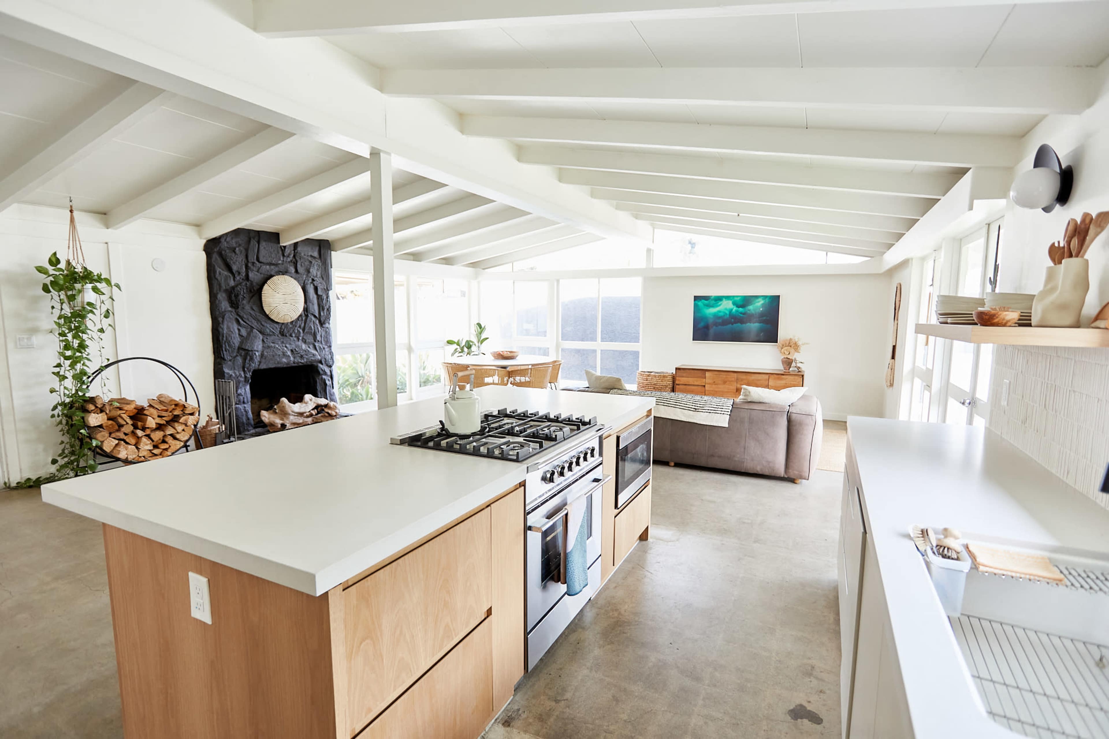 The image shows a modern, open-concept living space featuring a kitchen with an island and a living area adorned with a large stone fireplace and ample natural light.