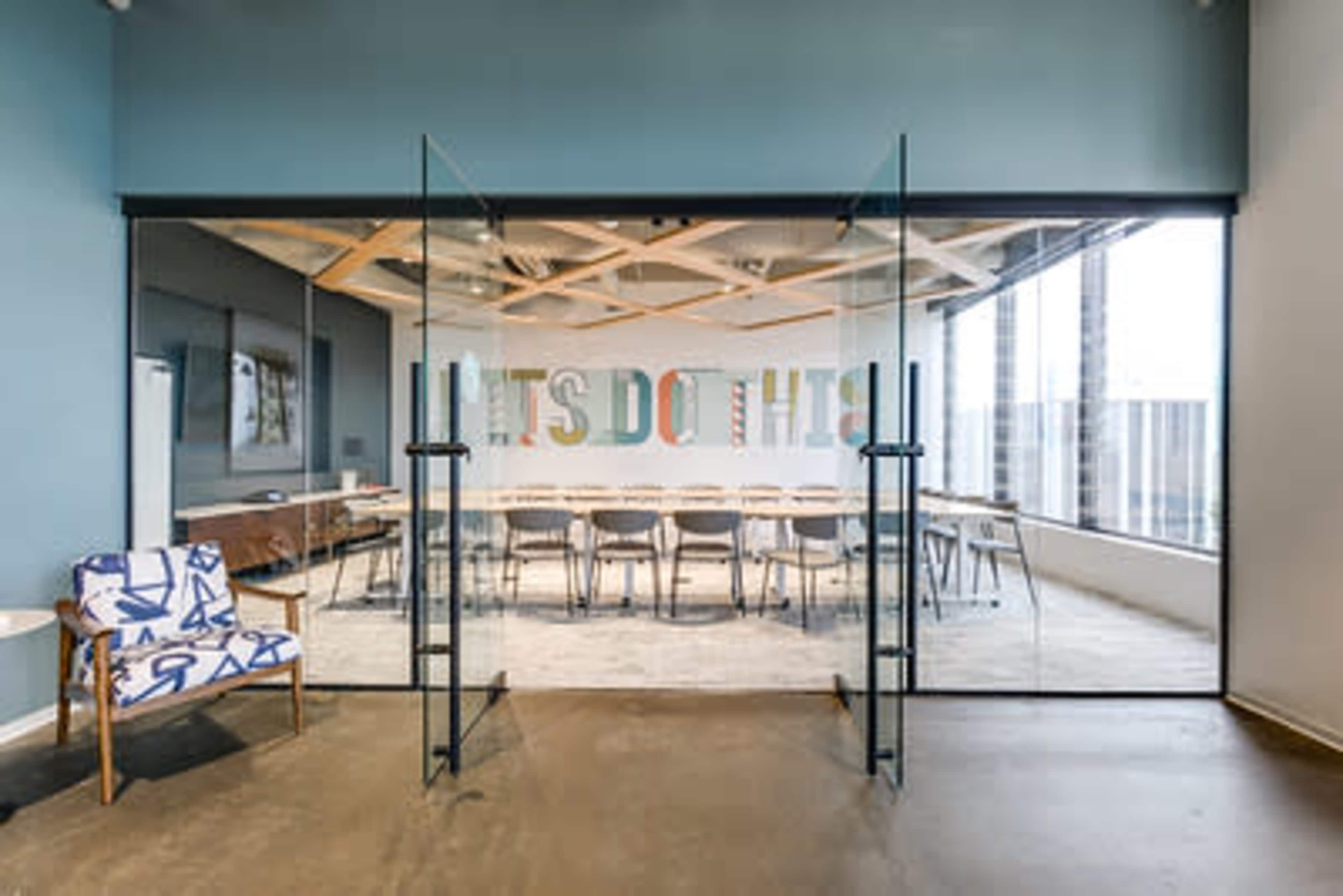 The image shows a large conference room with glass doors and a colorful sign reading "LET'S DO THIS" on the wall.