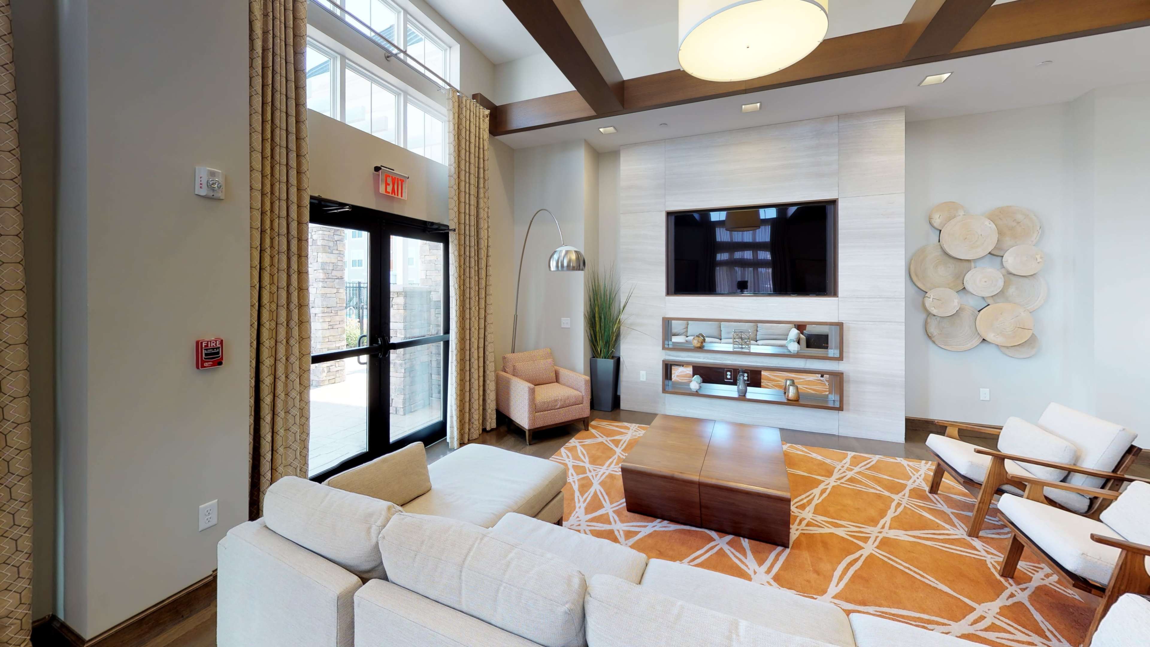 A modern lobby area with comfortable seating, a large television on the wall, and large windows allowing natural light to enter.