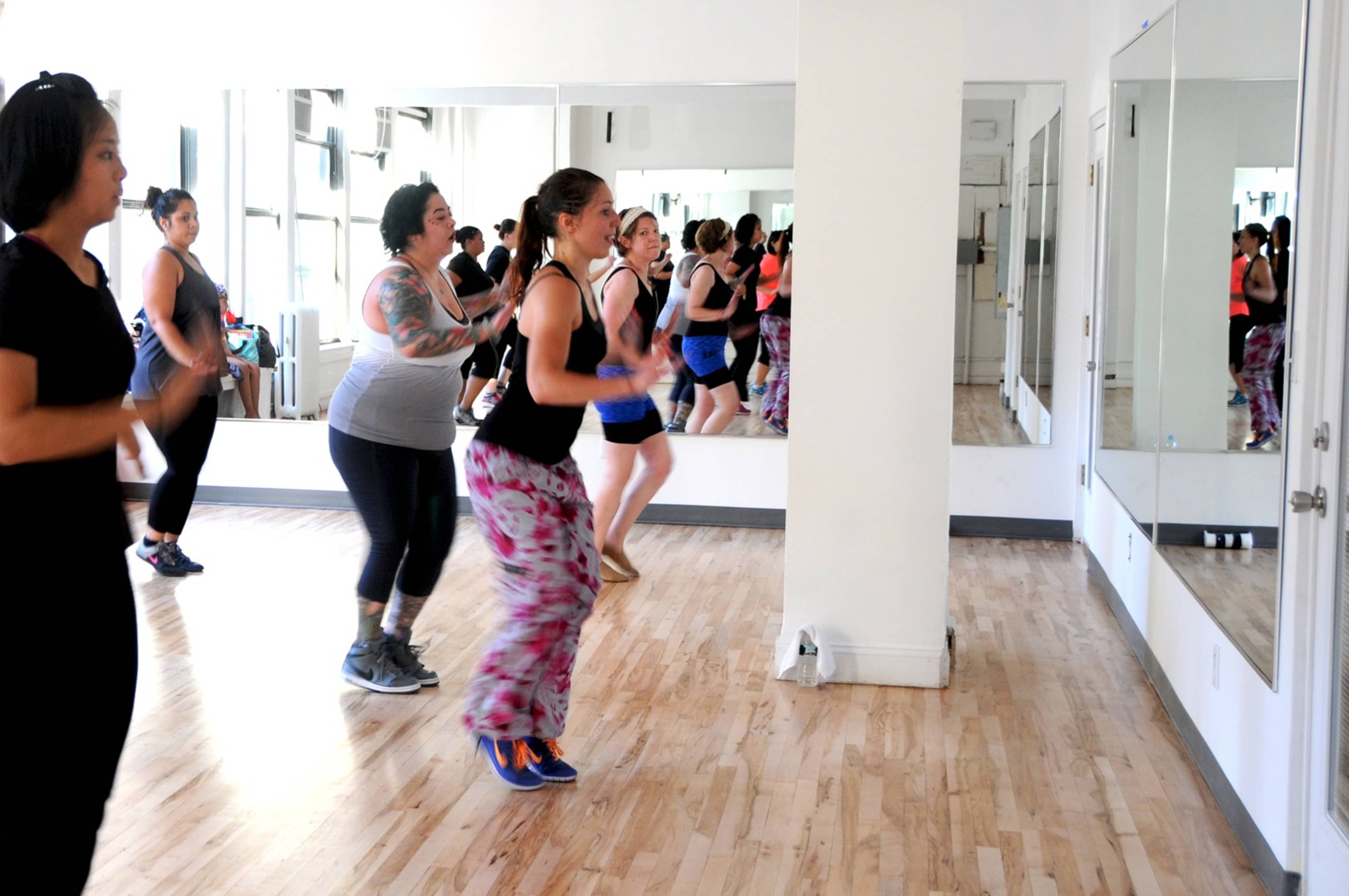 A group of women are participating in a dance class in a studio with mirrors and wooden floors.