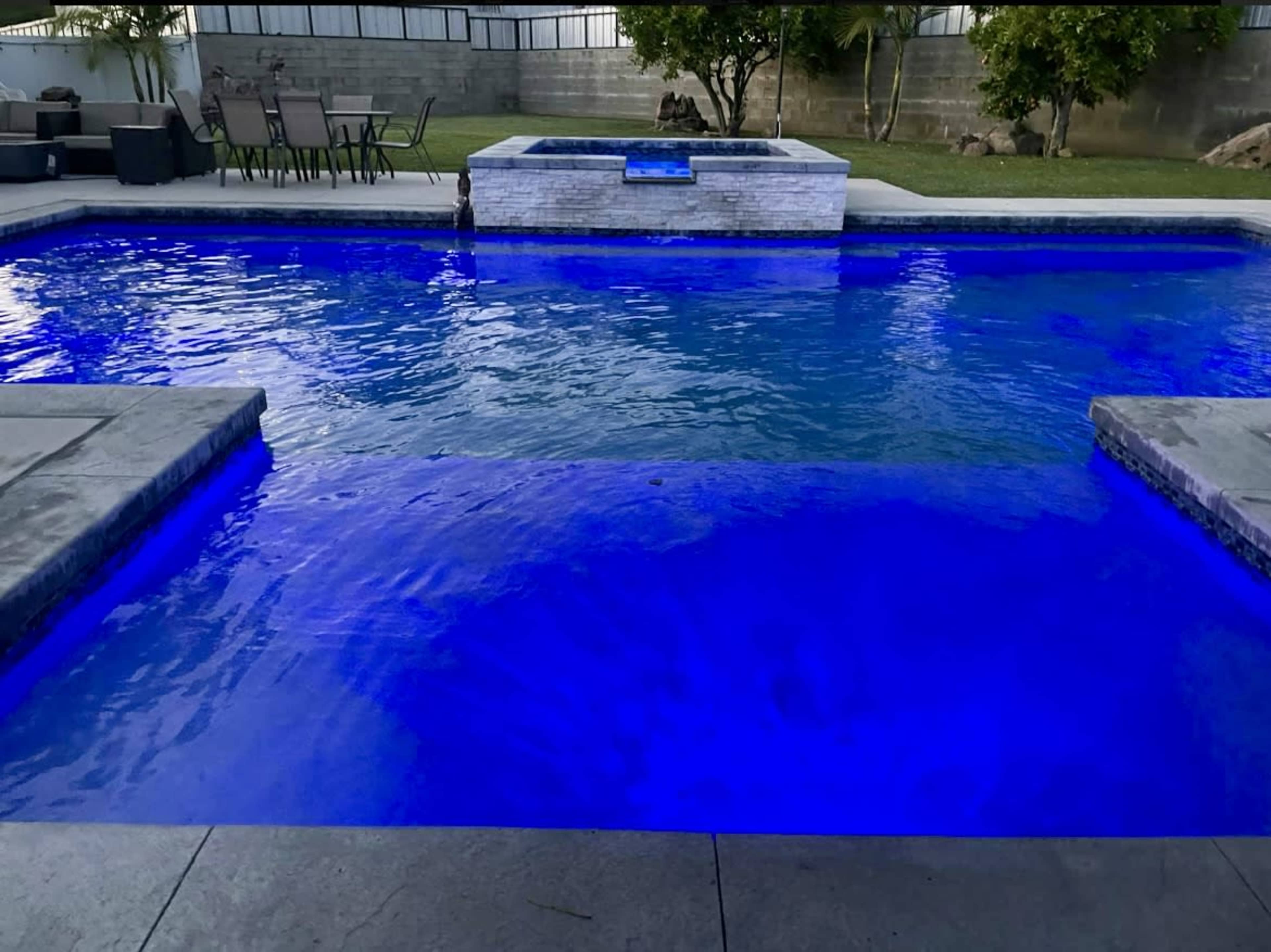 A swimming pool with blue lighting, surrounded by concrete and grass areas.