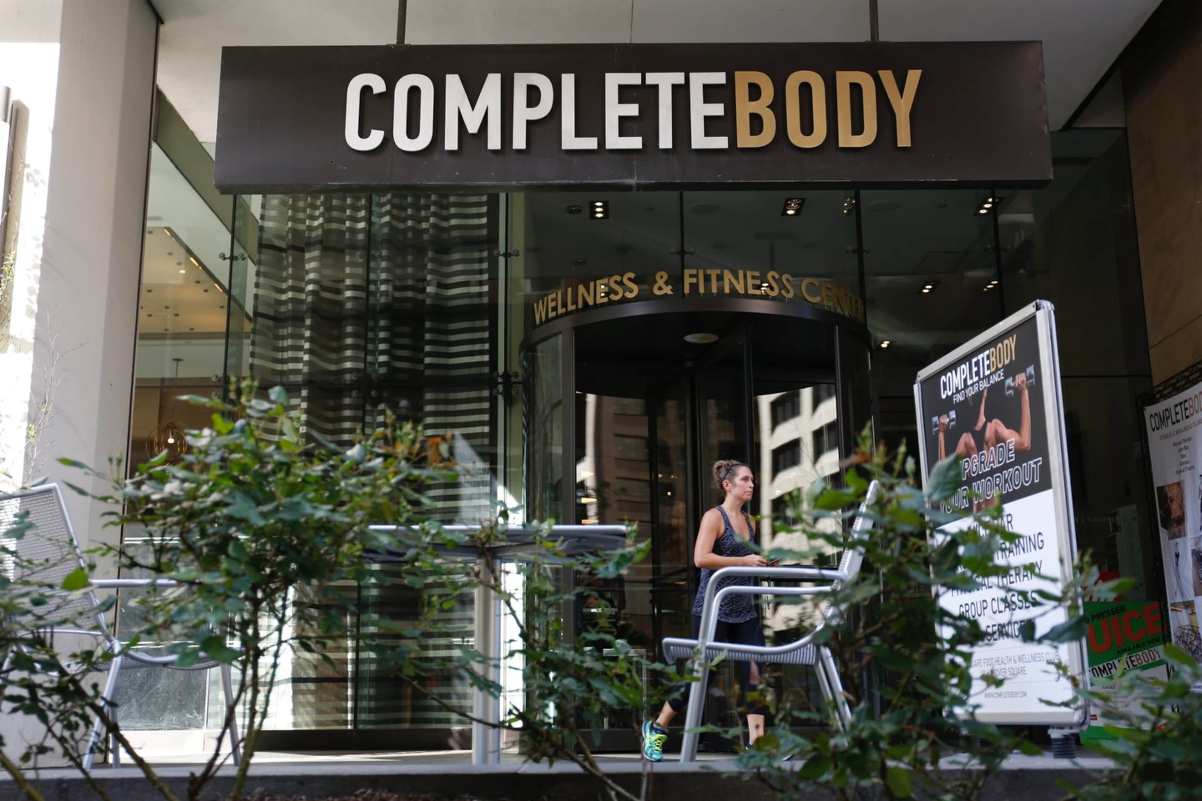 A woman jogs past the entrance of the Complete Body Wellness & Fitness Center, which features large signage above the entrance.