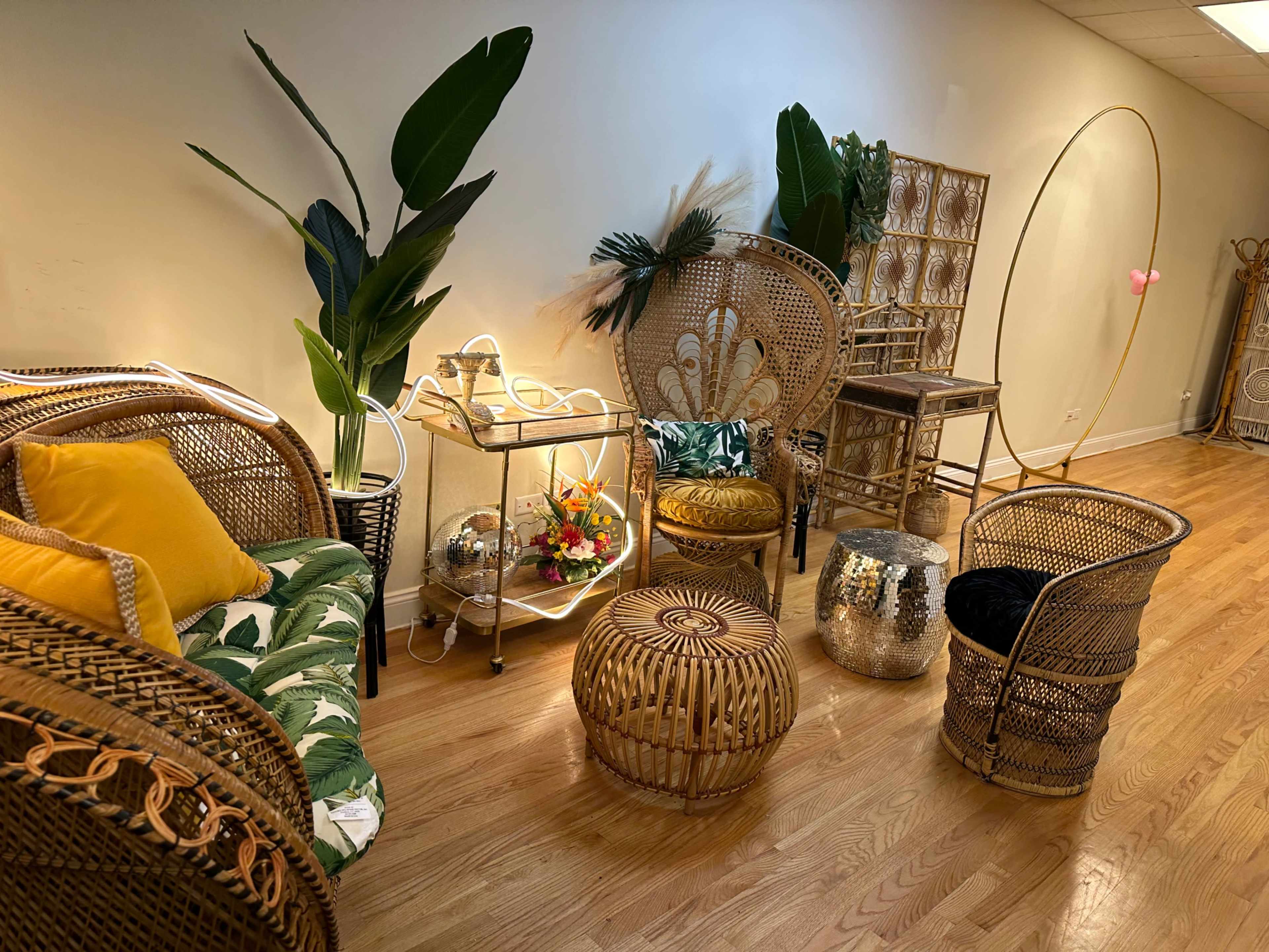The image shows a cozy seating area featuring rattan furniture, decorative plants, and a mix of colorful cushions and accessories.
