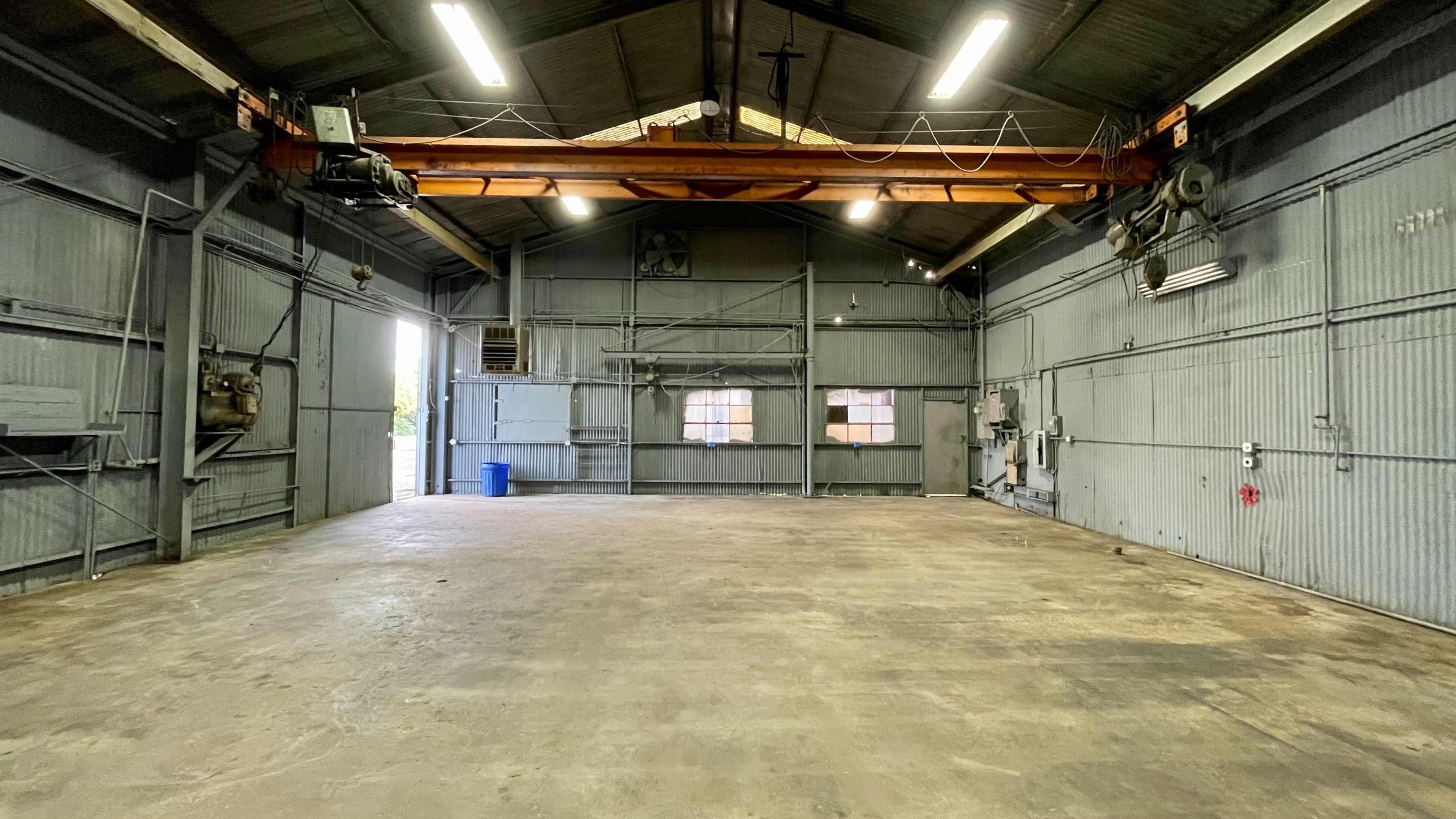 An empty industrial warehouse with a high ceiling, overhead crane, and concrete floor.