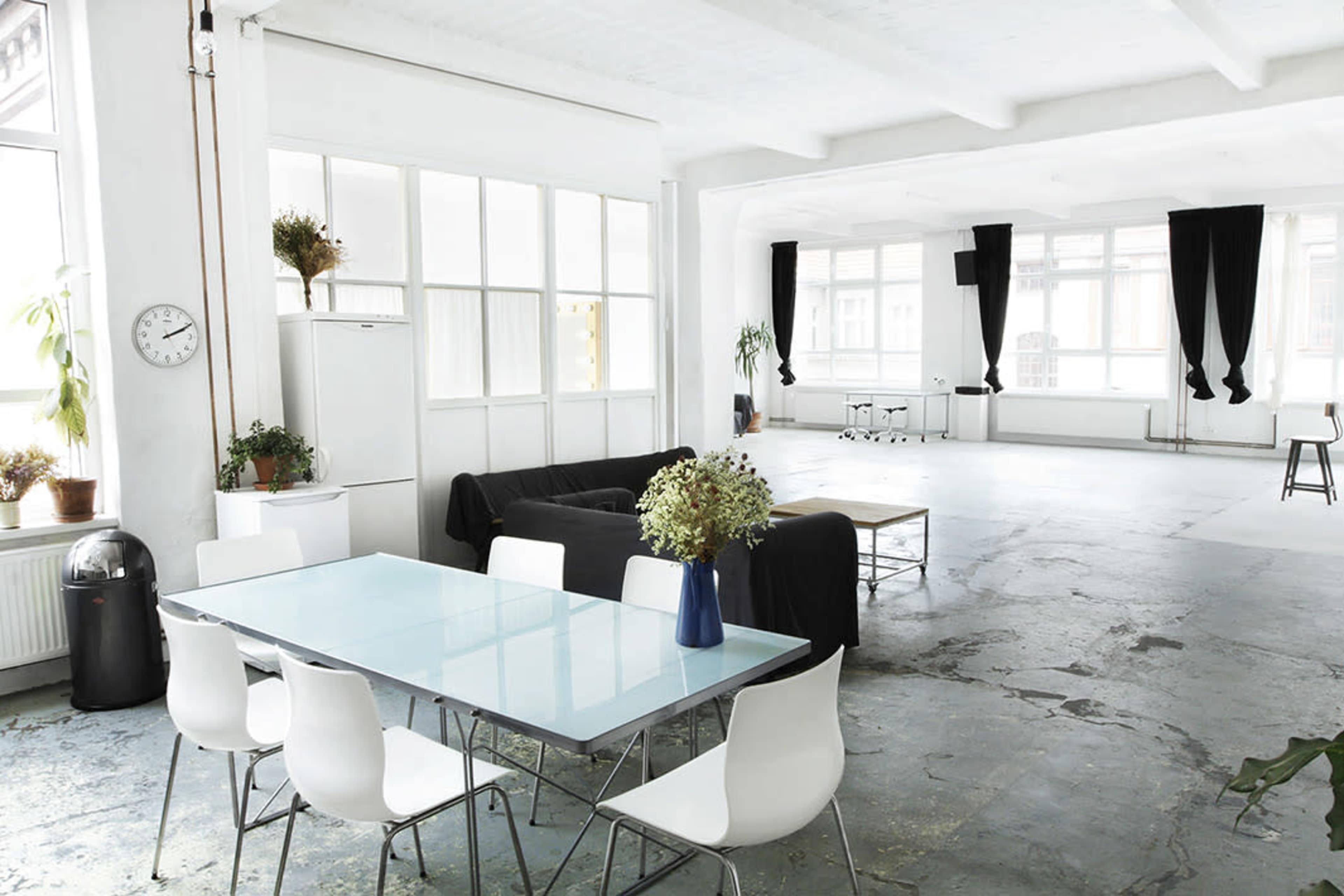 A spacious, modern room featuring a dining table with chairs, a black couch, and large windows providing ample natural light.