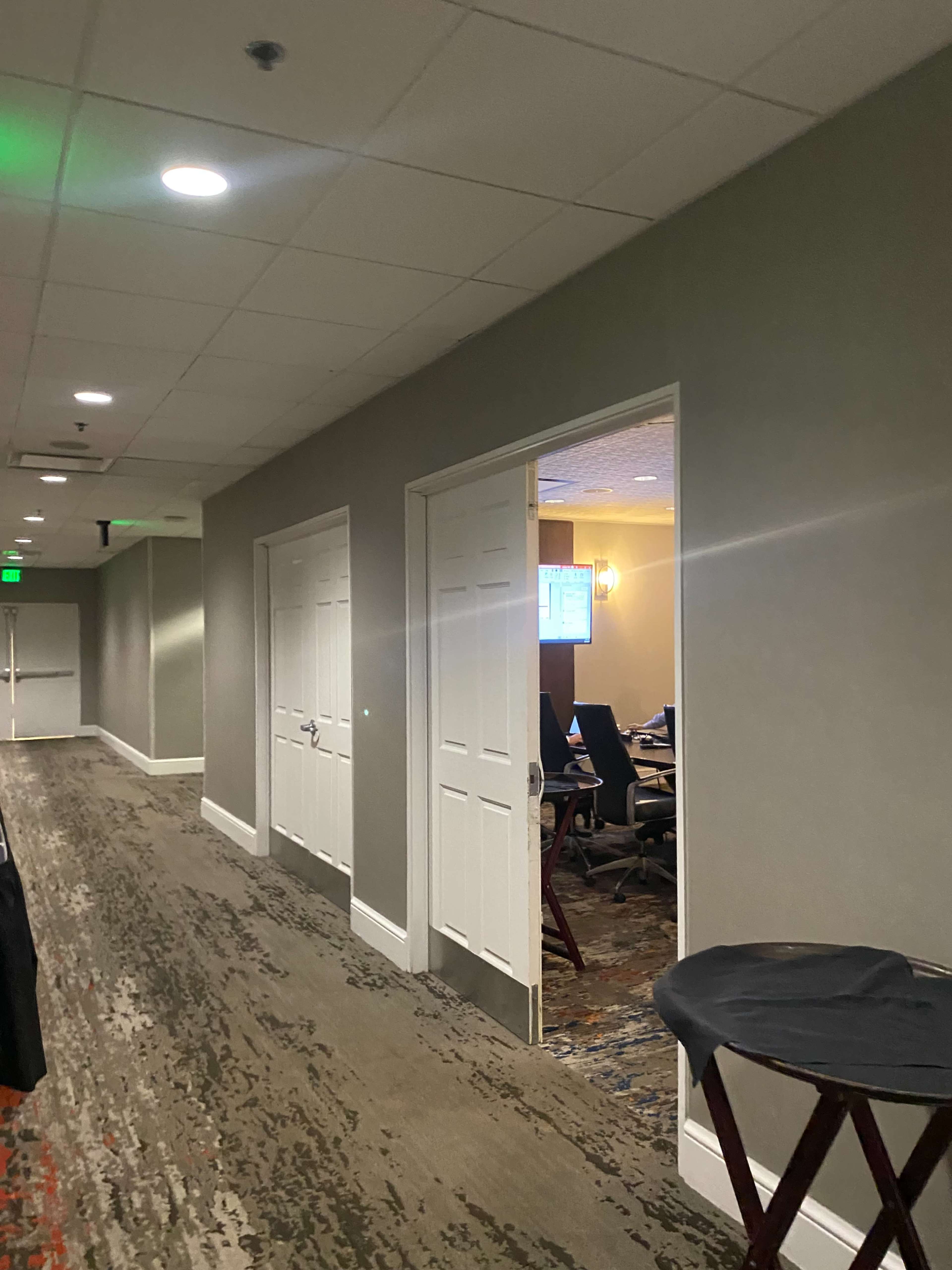 A hallway features a series of closed doors leading to a conference room with tables and chairs visible through an open doorway.