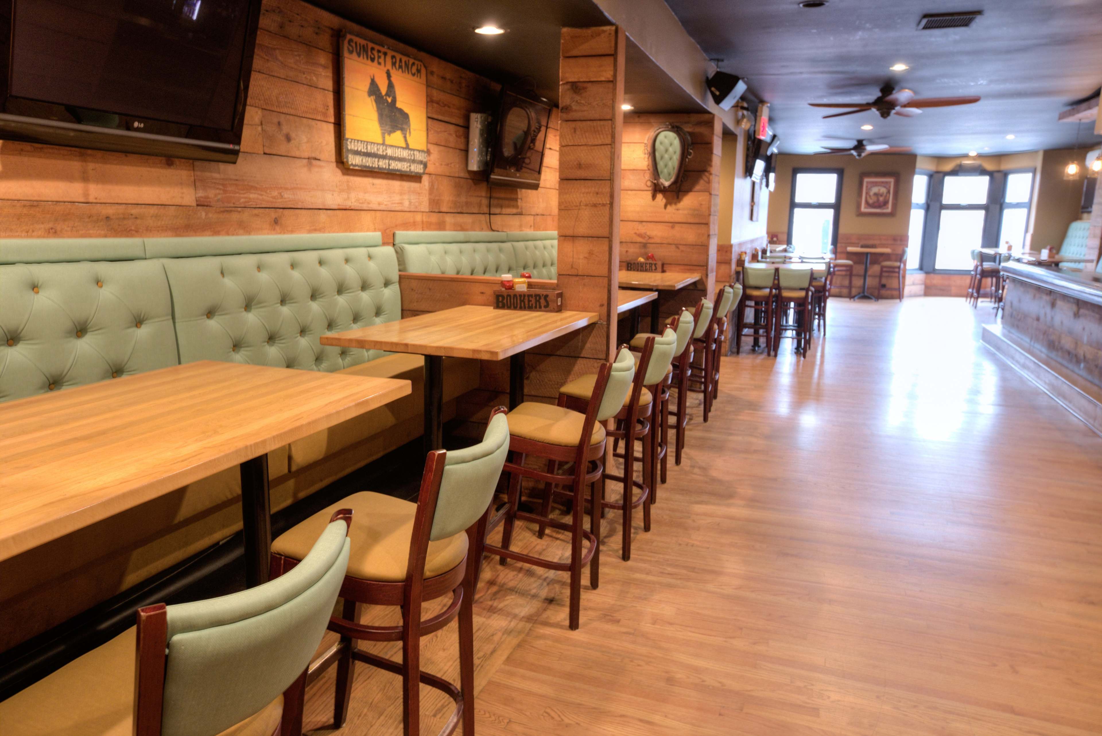 The image shows a spacious restaurant with wooden walls, green cushioned booths, and wooden tables arranged in a linear layout.