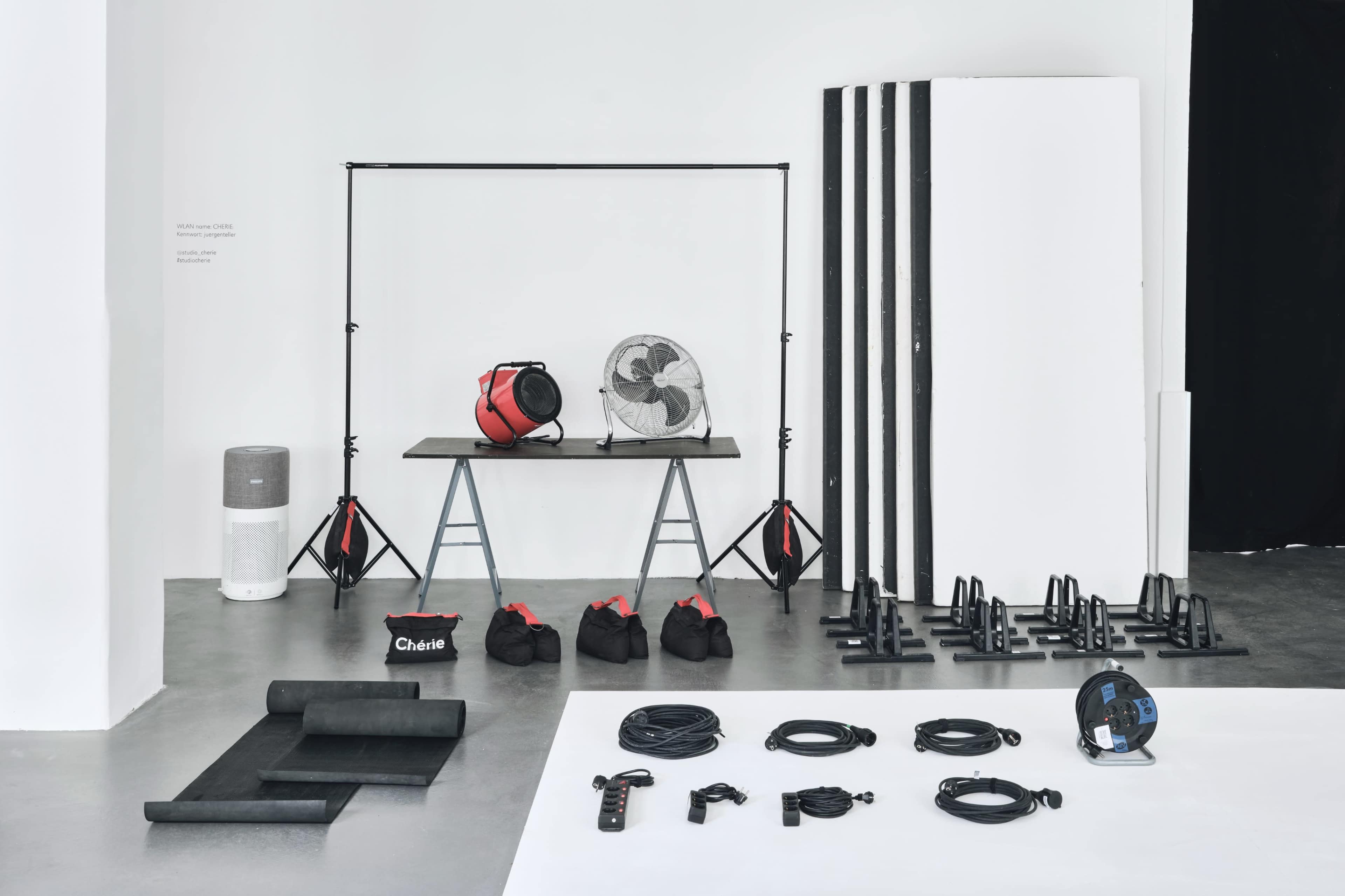 The image shows an arrangement of workout equipment, including weights, resistance bands, a fan, and exercise mats, on a minimalist background.